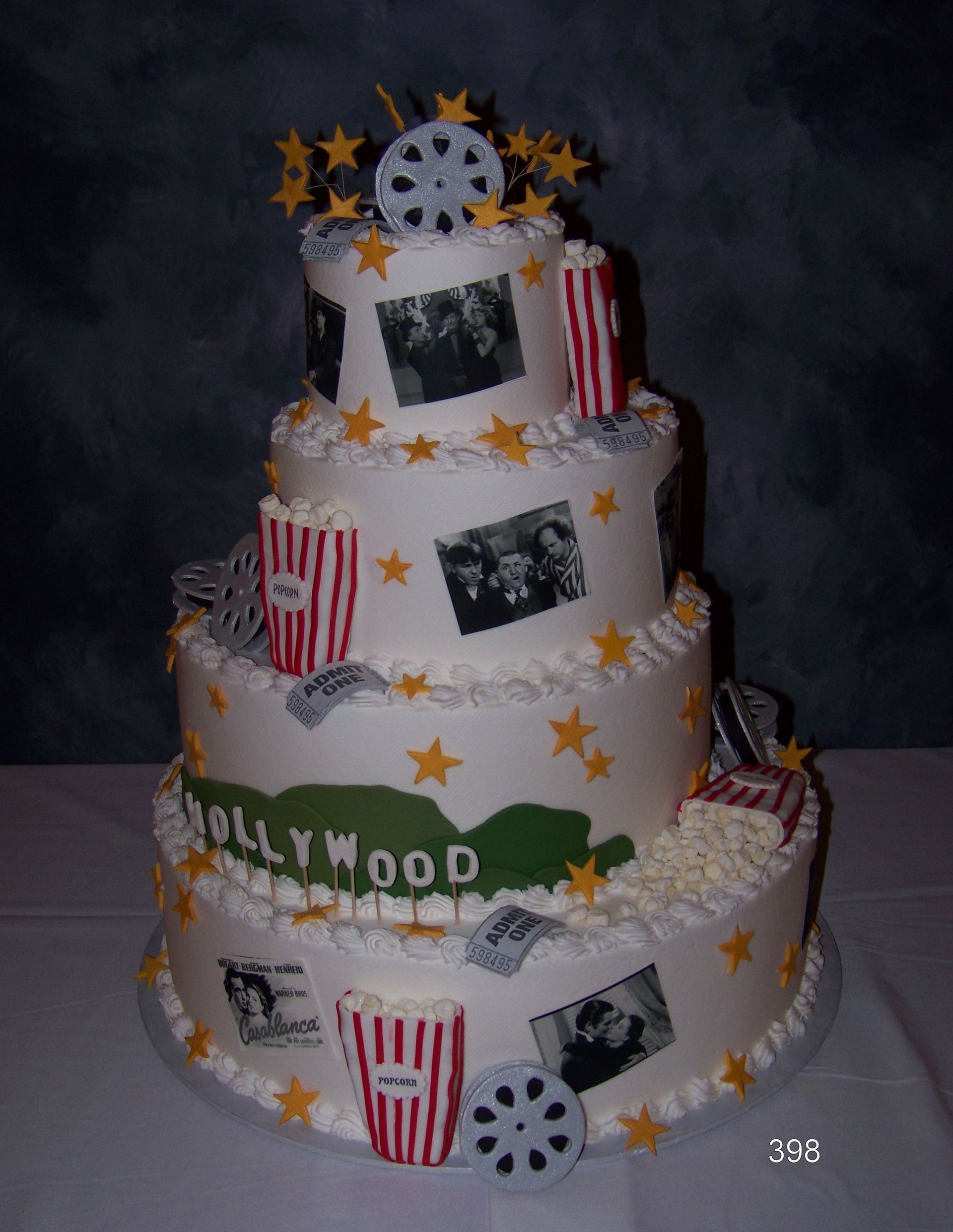 Decorated white tiered cake with film-themed accents, red striped boxes, stars, and “Hollywood” text