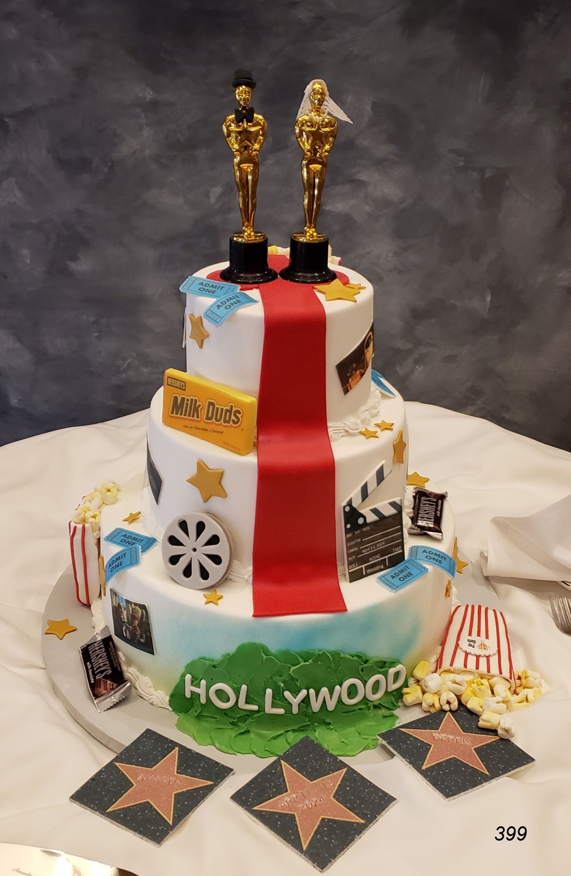 Hollywood-themed tiered cake with red drape, gold Oscars, and film reel decorations