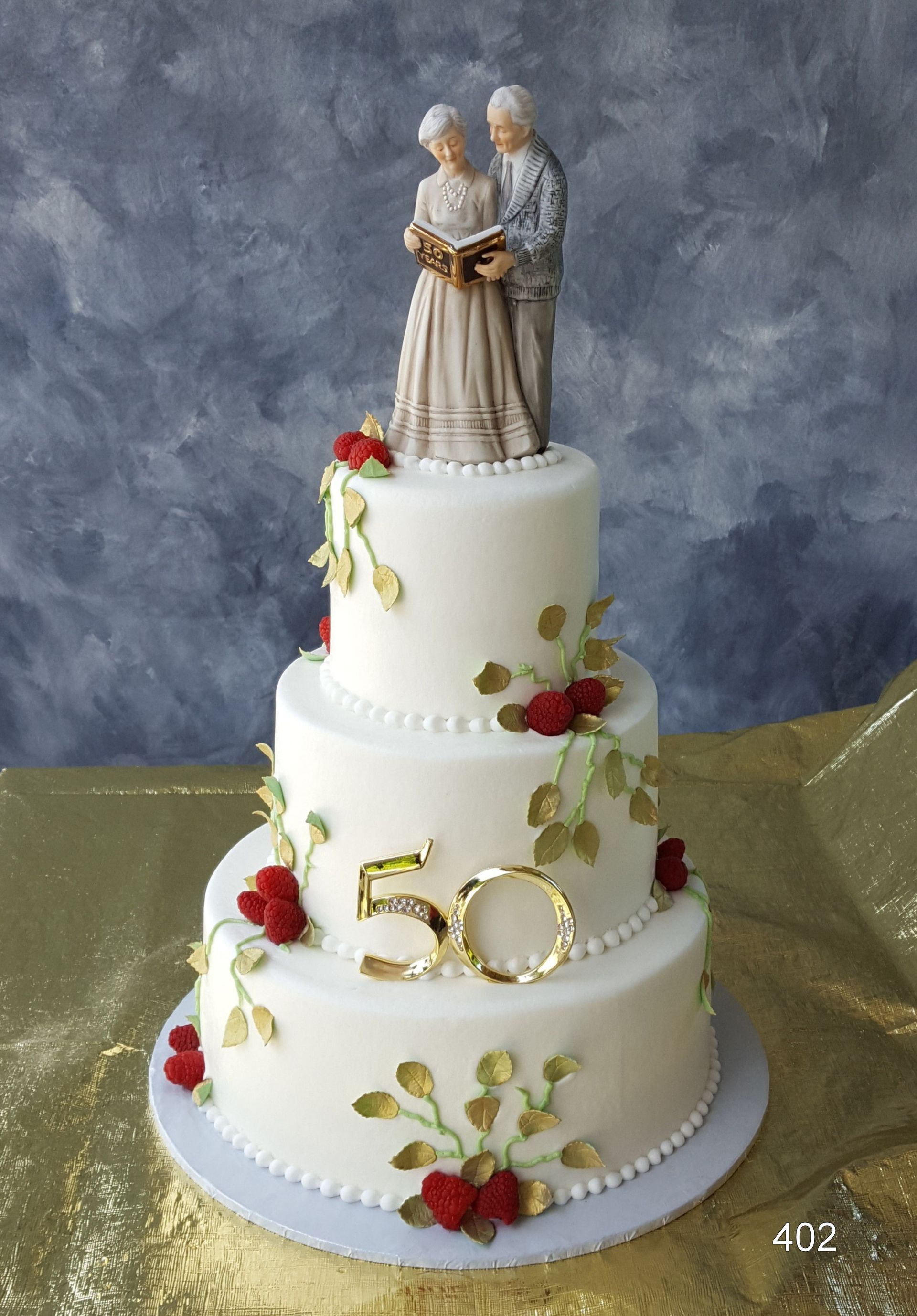 Three-tier white wedding cake with gold and red floral accents and a bride and groom topper