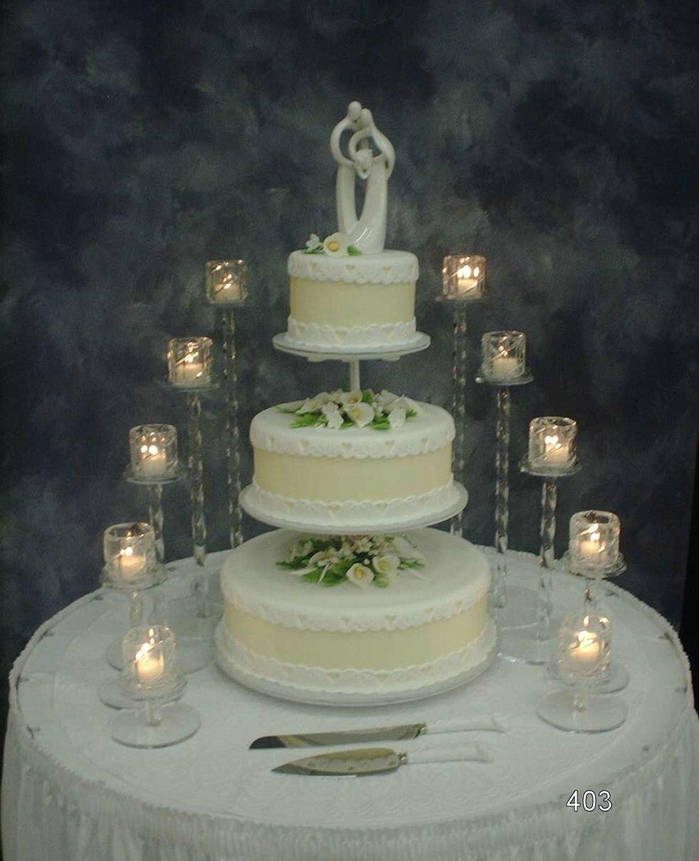 Three-tier white wedding cake with floral accents and candles on a round table