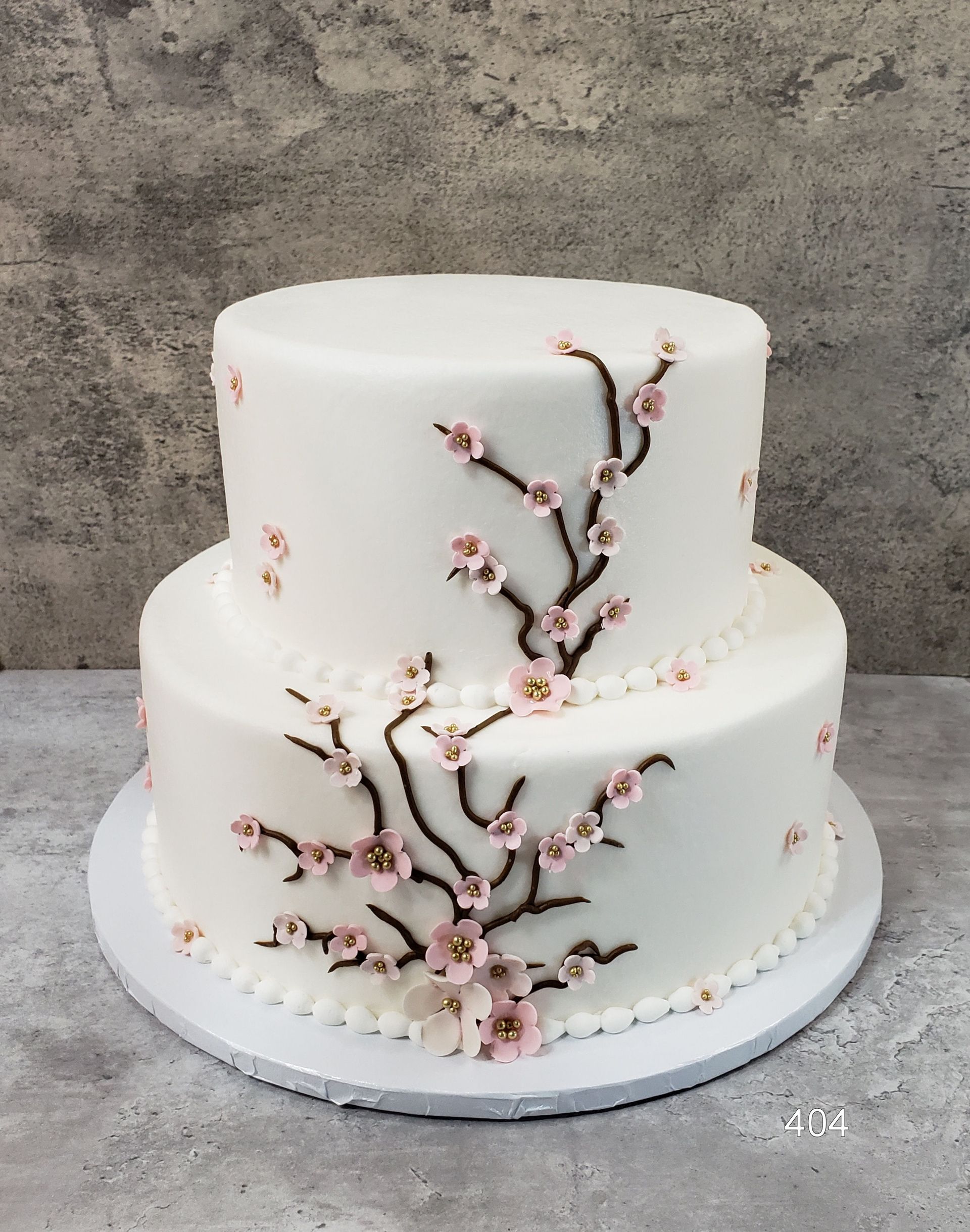 Two-tier white cake with pink cherry blossom branch decoration on a white cake board