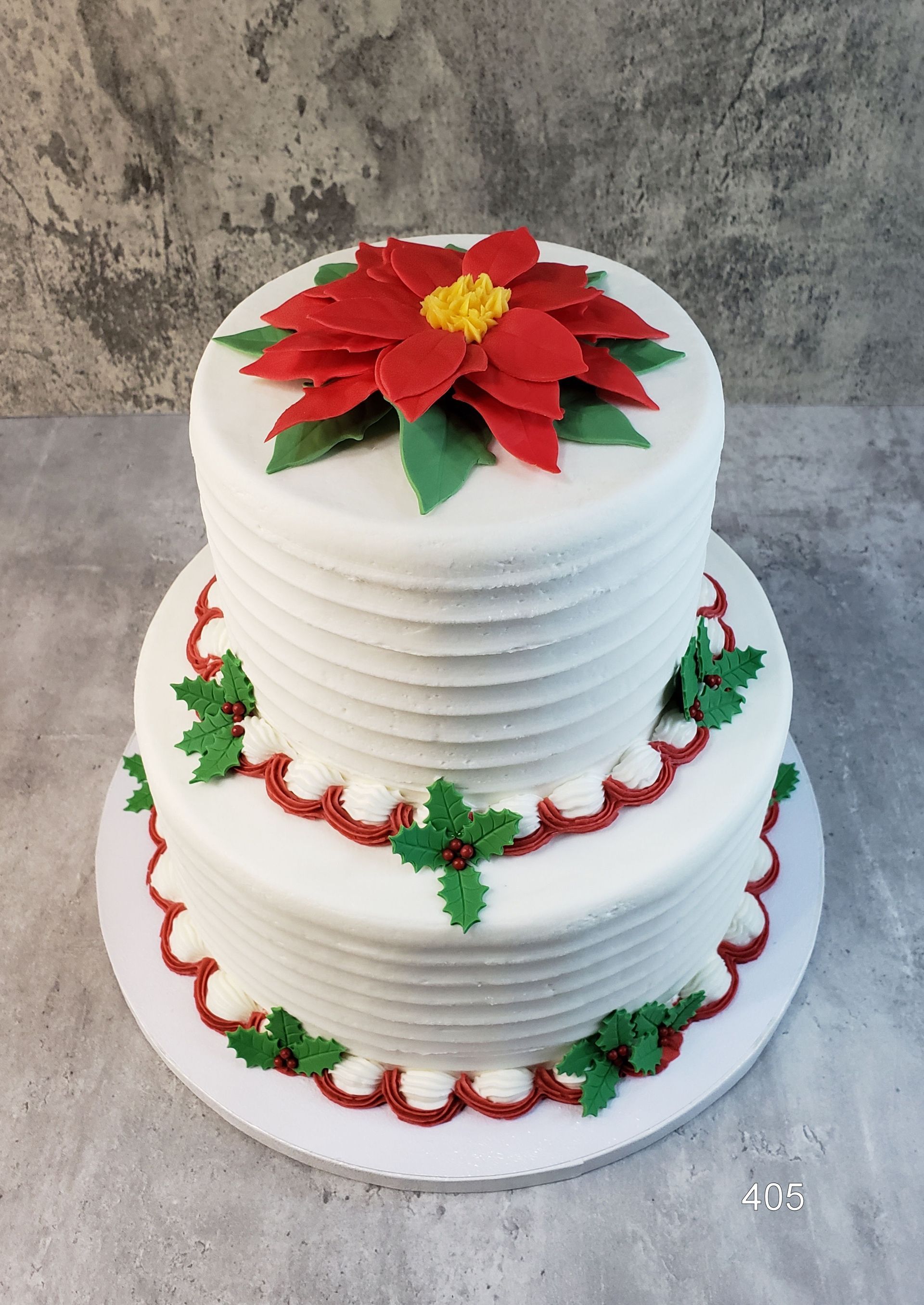 Three-tier white cake with red poinsettia and green leaf decorations on a gray background