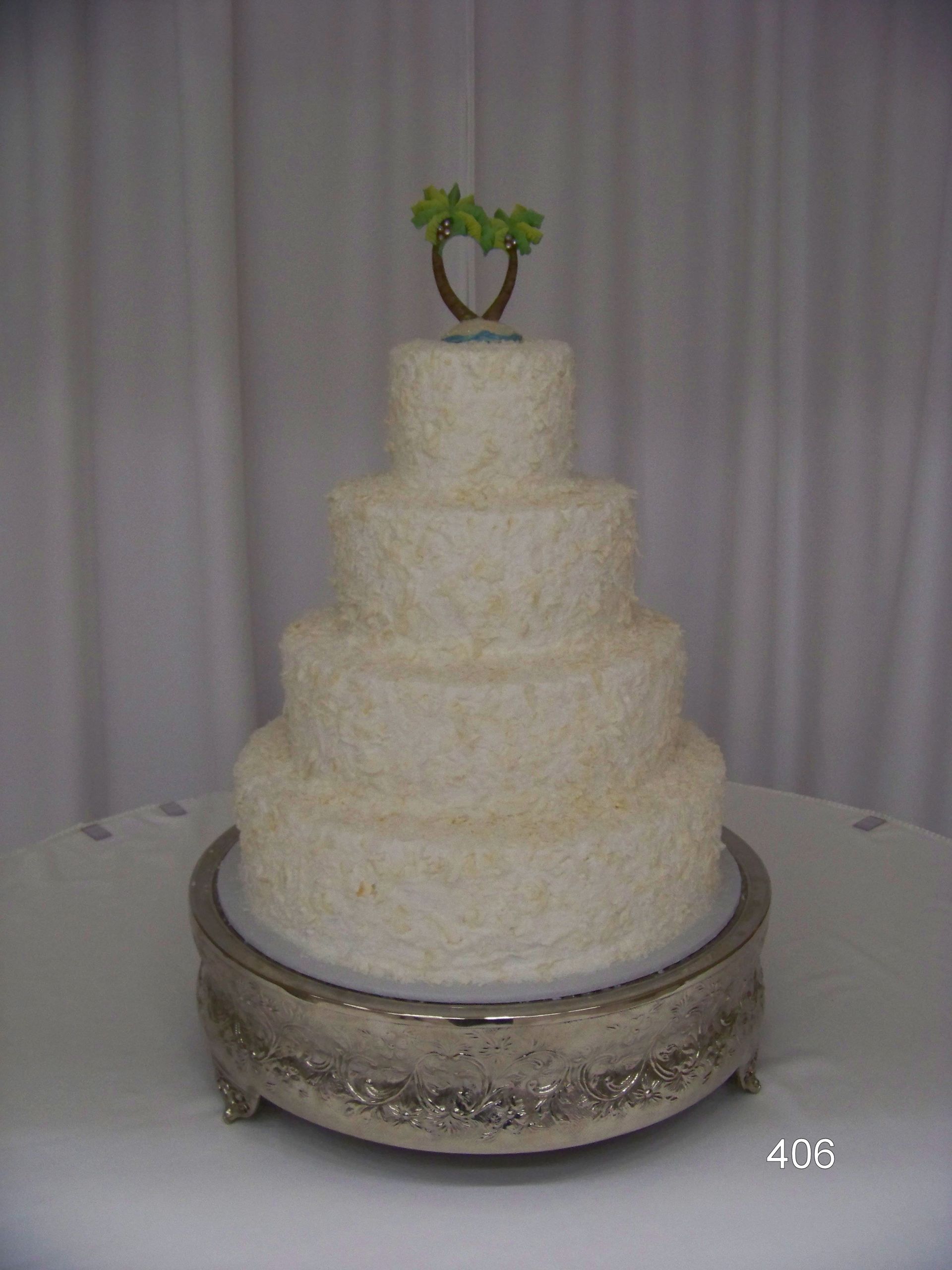 Four-tier white wedding cake on a silver stand, topped with a small green plant