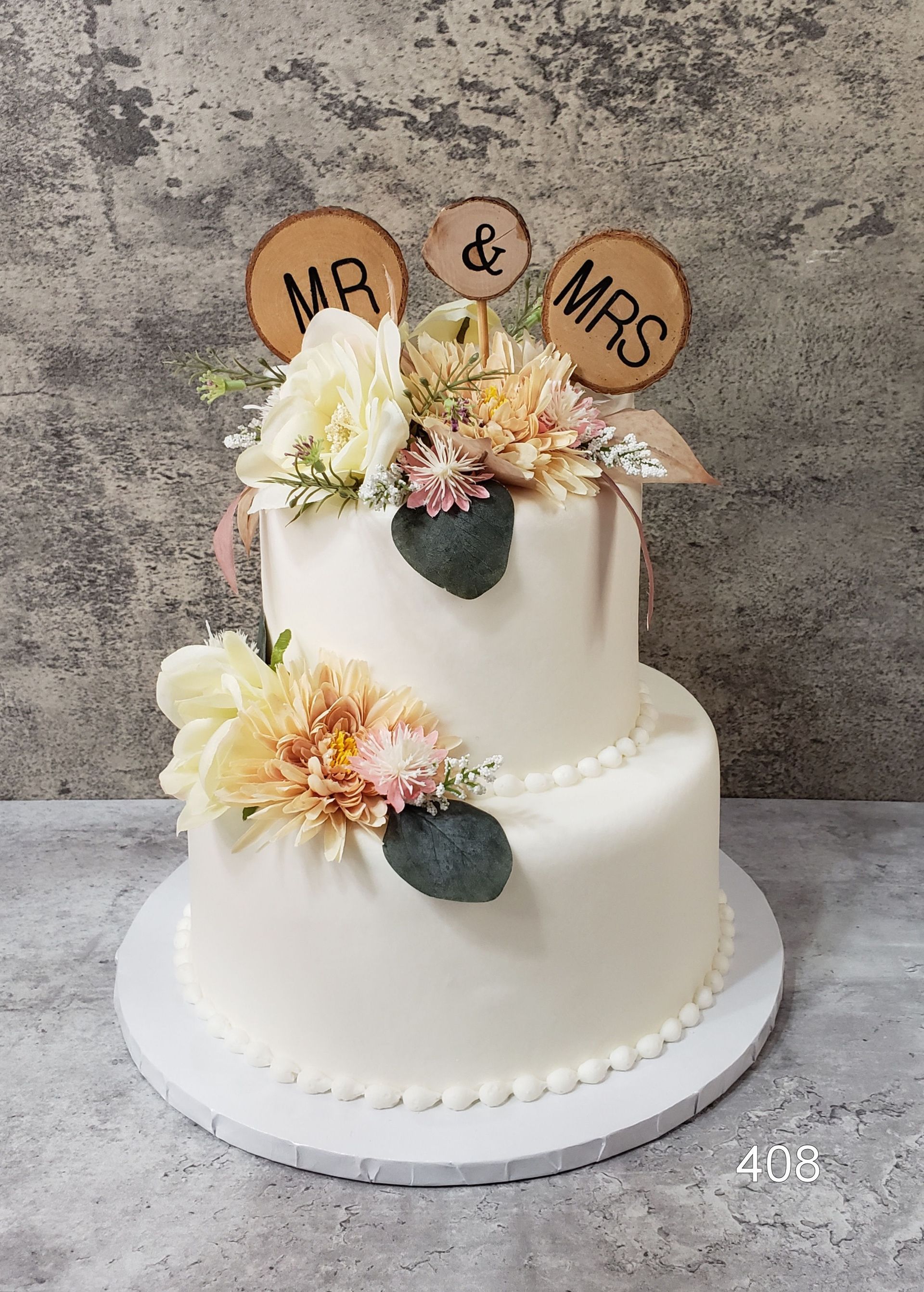 Two-tier white cake with peach flowers and gold toppers reading “Mr & Mrs”