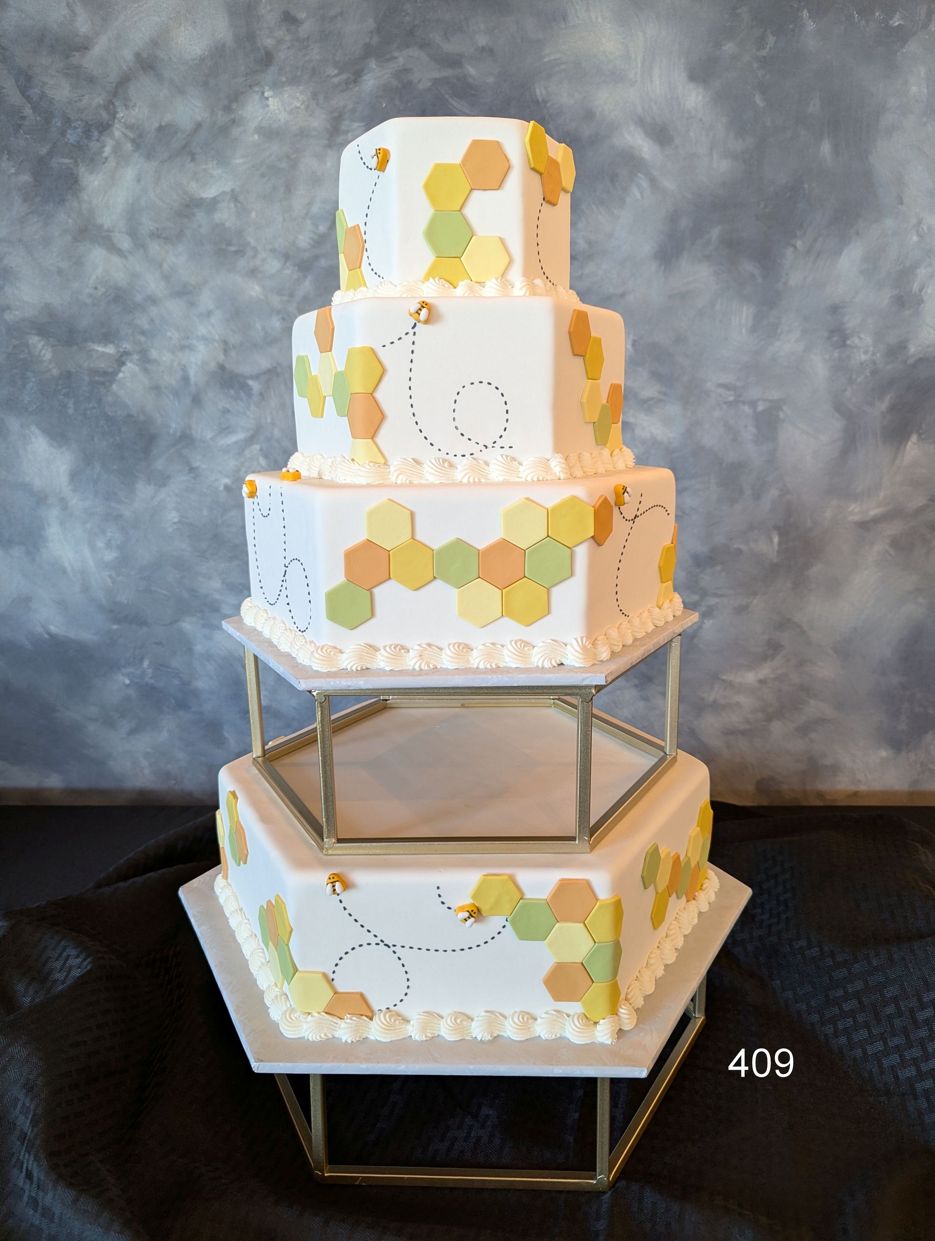 Five-tier white cake with pastel hexagon accents on a gold geometric stand