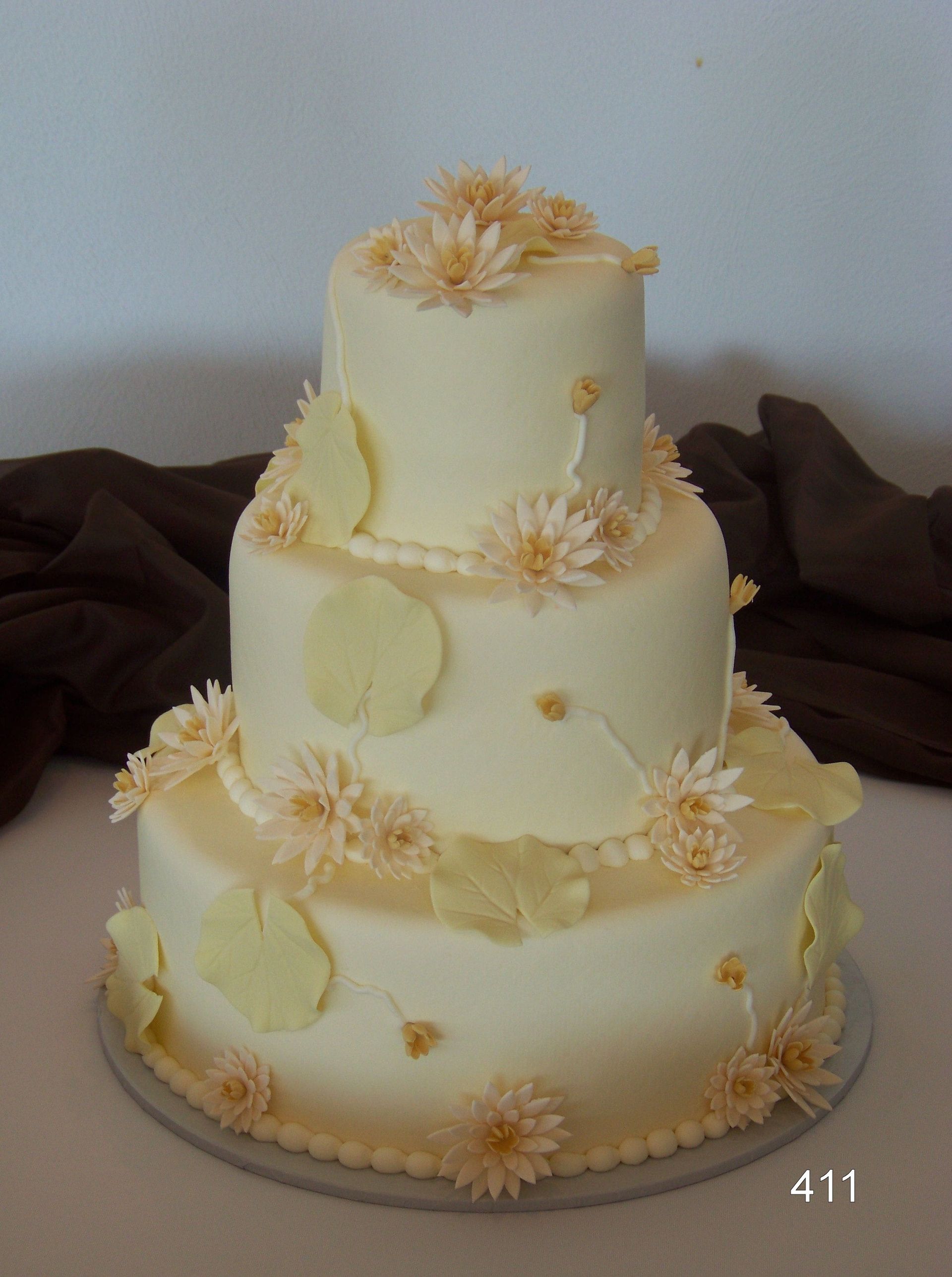 Three-tier white wedding cake with pale yellow flowers and leaves on a table