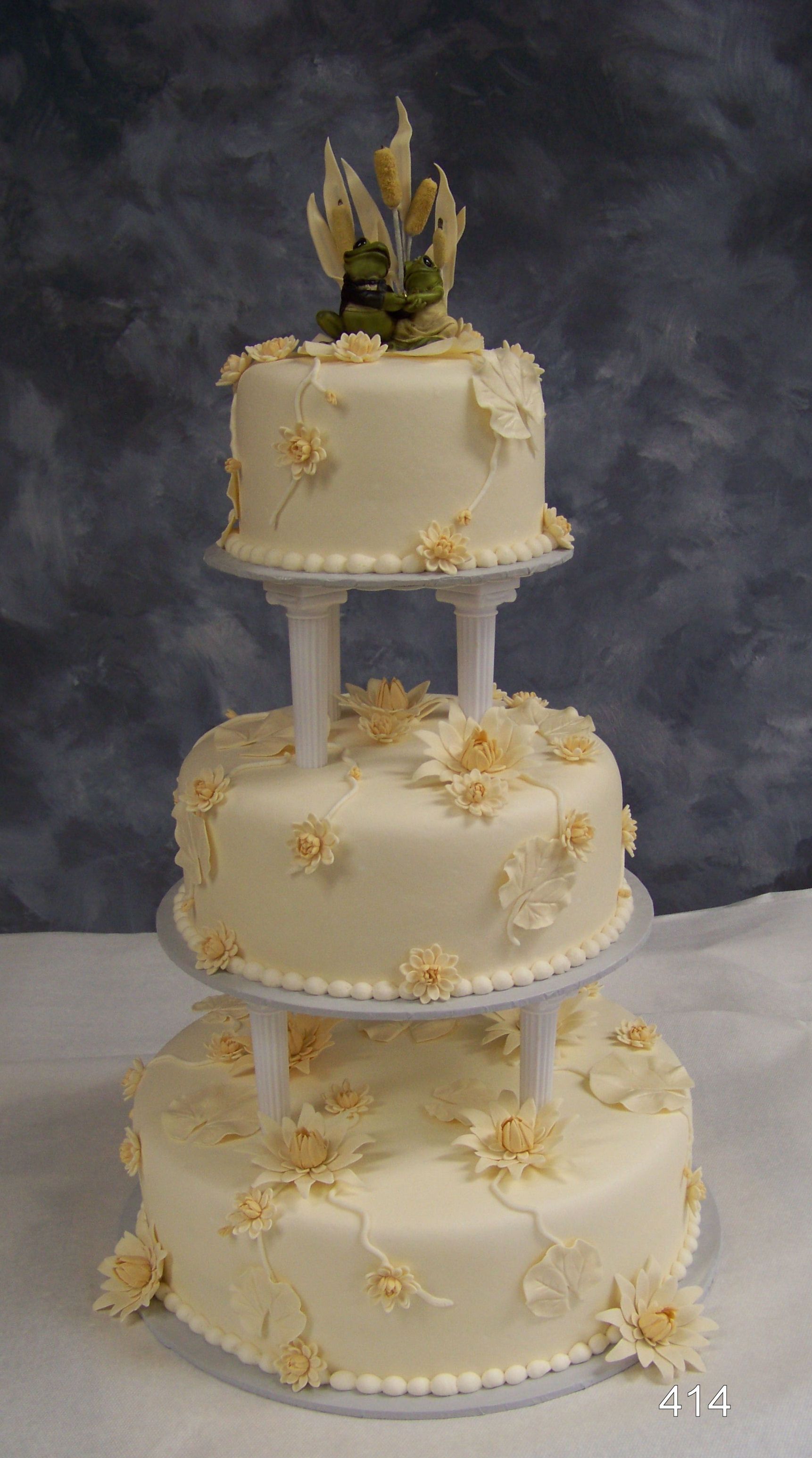Three-tier white wedding cake with floral decorations and a small floral topper on a gray backdrop