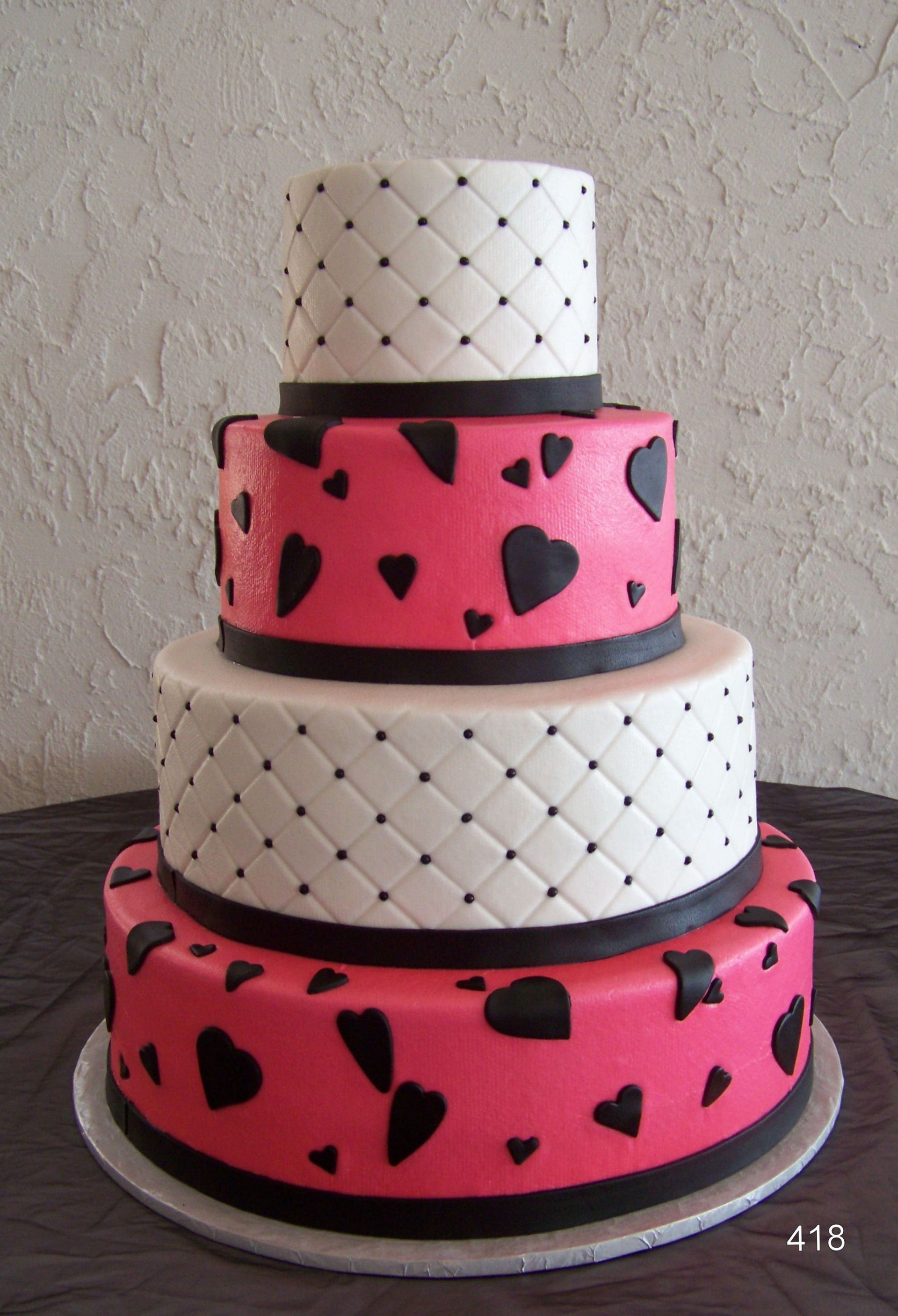 Three-tier pink and white cake with black hearts and quilted patterns on a cake board
