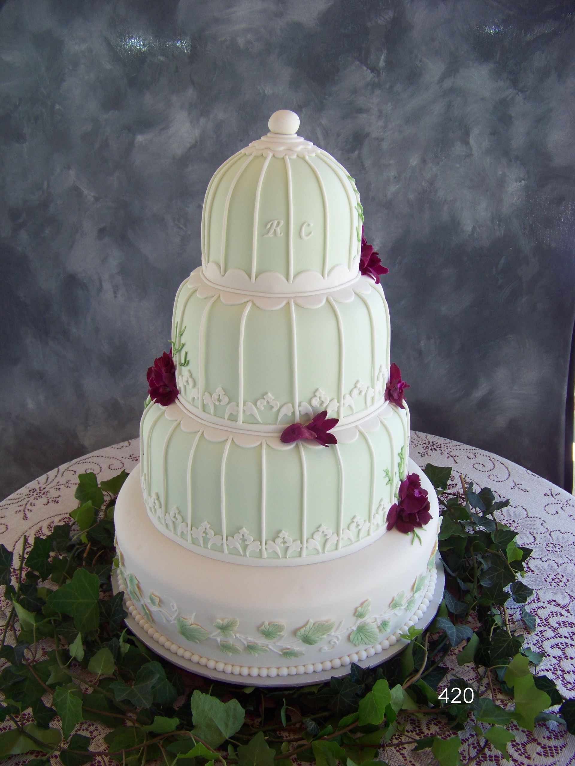 Three-tier mint green and white cake with floral accents on a stand against a dark backdrop