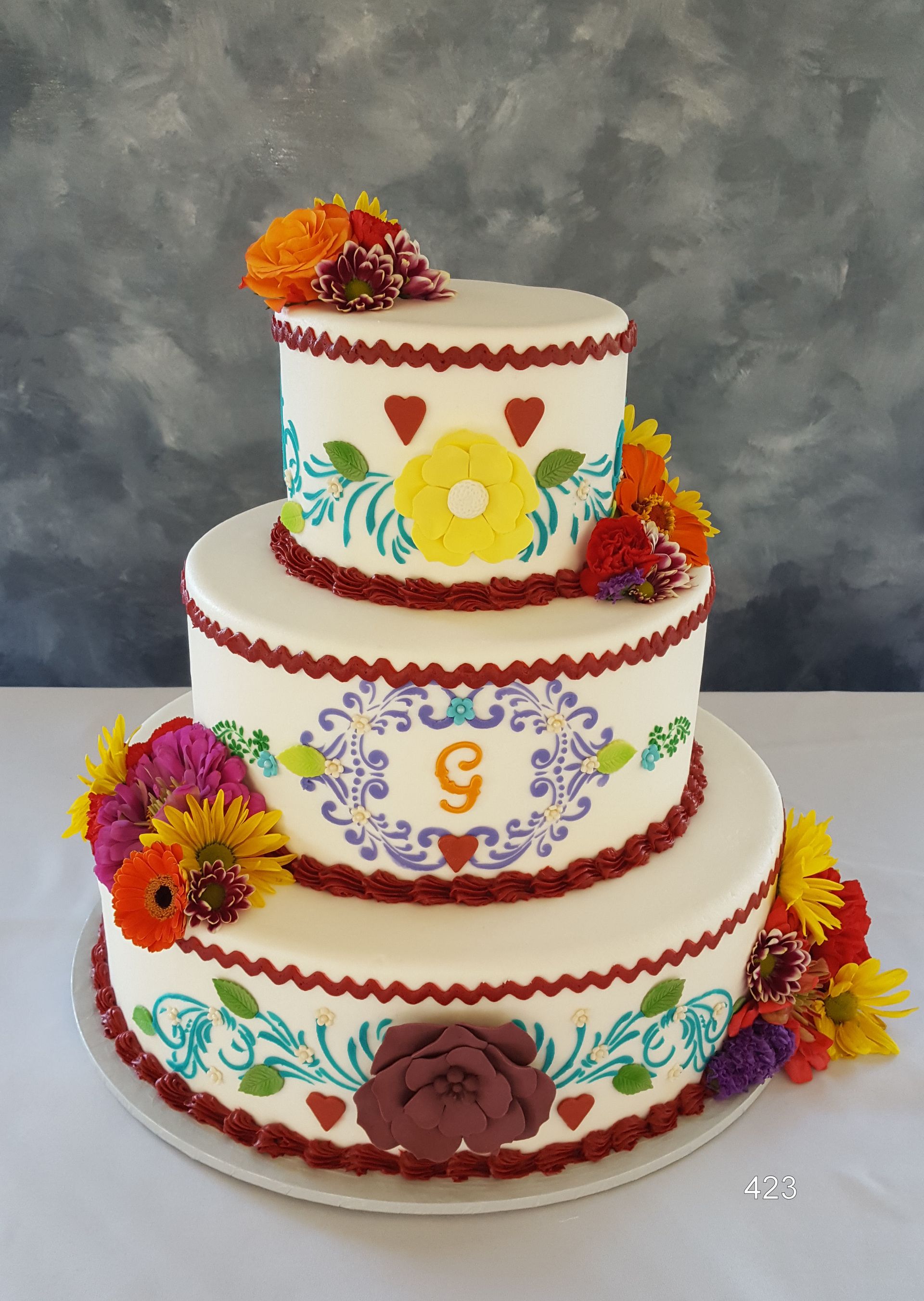 Three-tier white cake with colorful floral icing and orange flower decorations on a gray backdrop