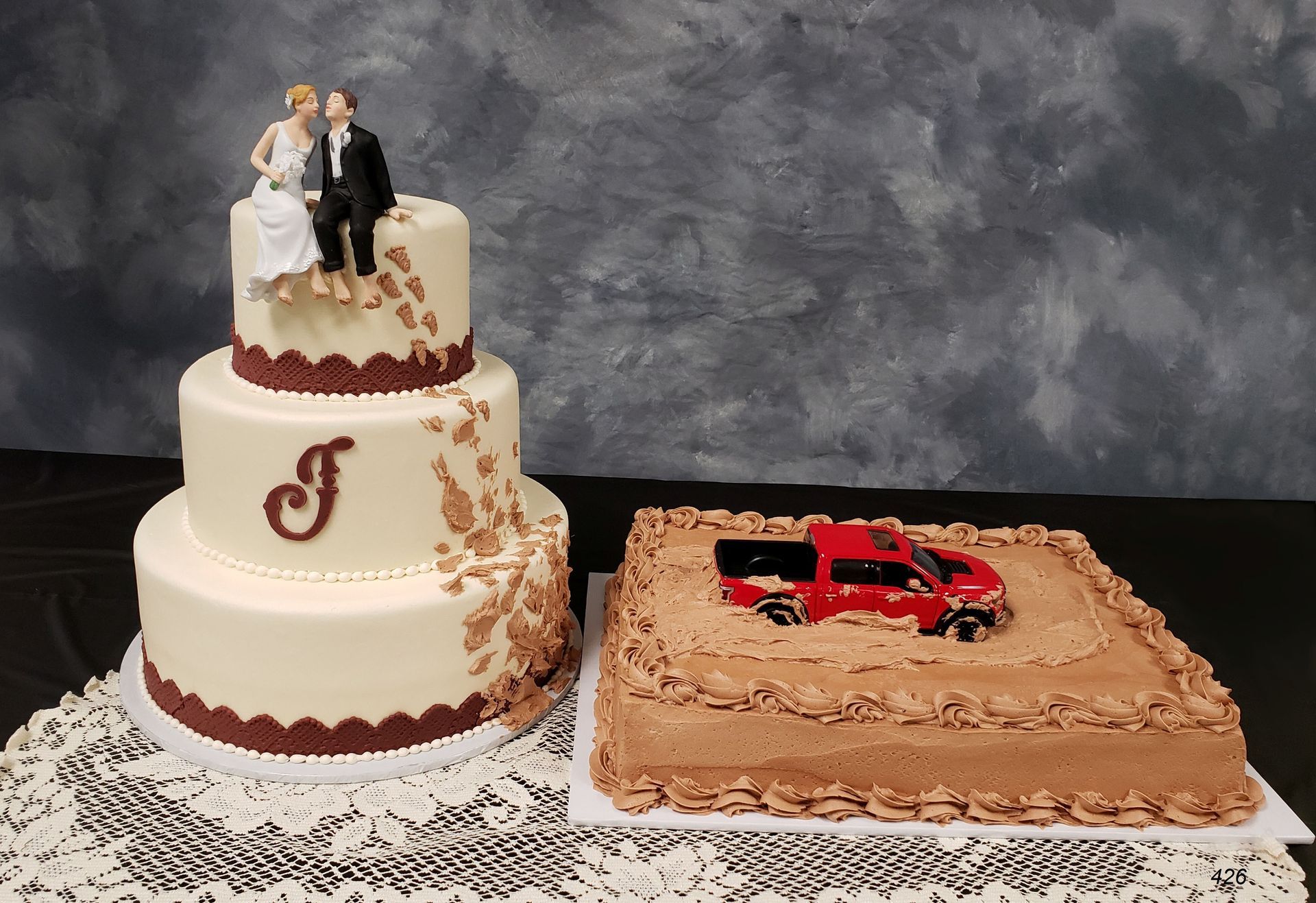 Wedding cake with bride and groom topper beside a red truck cake on a table