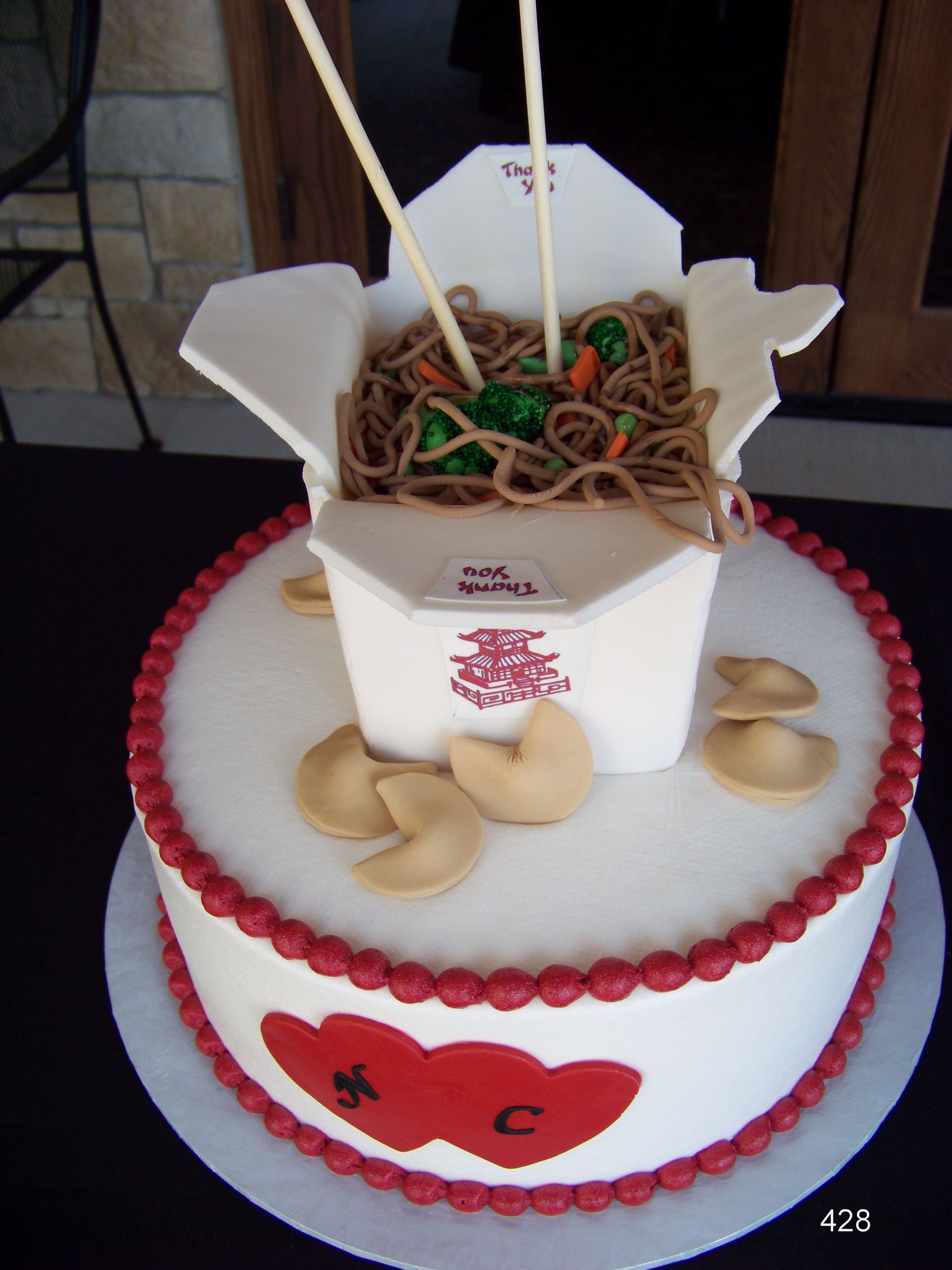 Two-tier cake with takeout box and noodles, fortune cookies, and red trim on white frosting