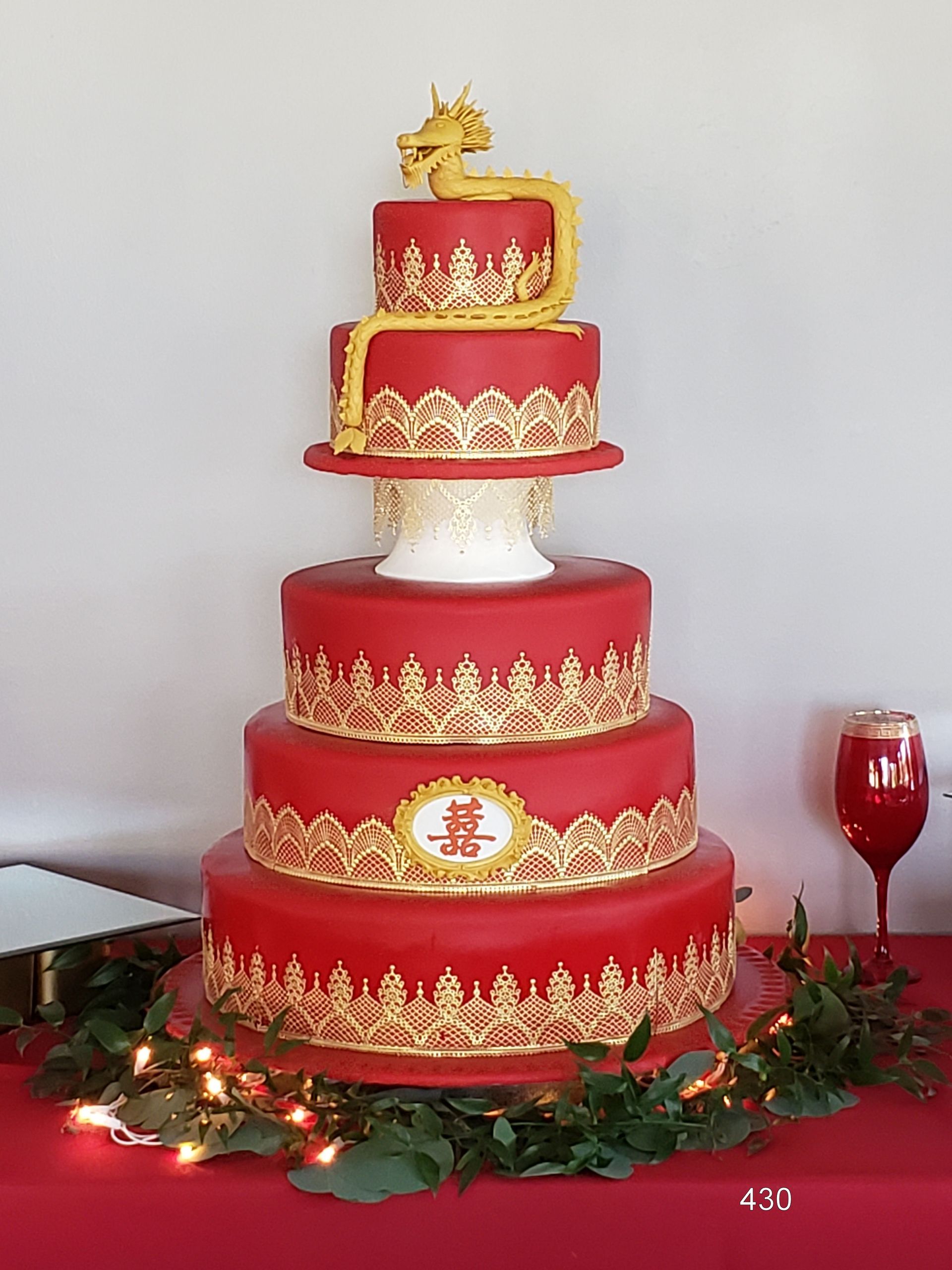 Red and gold multi-tiered wedding cake with floral decorations and a golden topper on a table