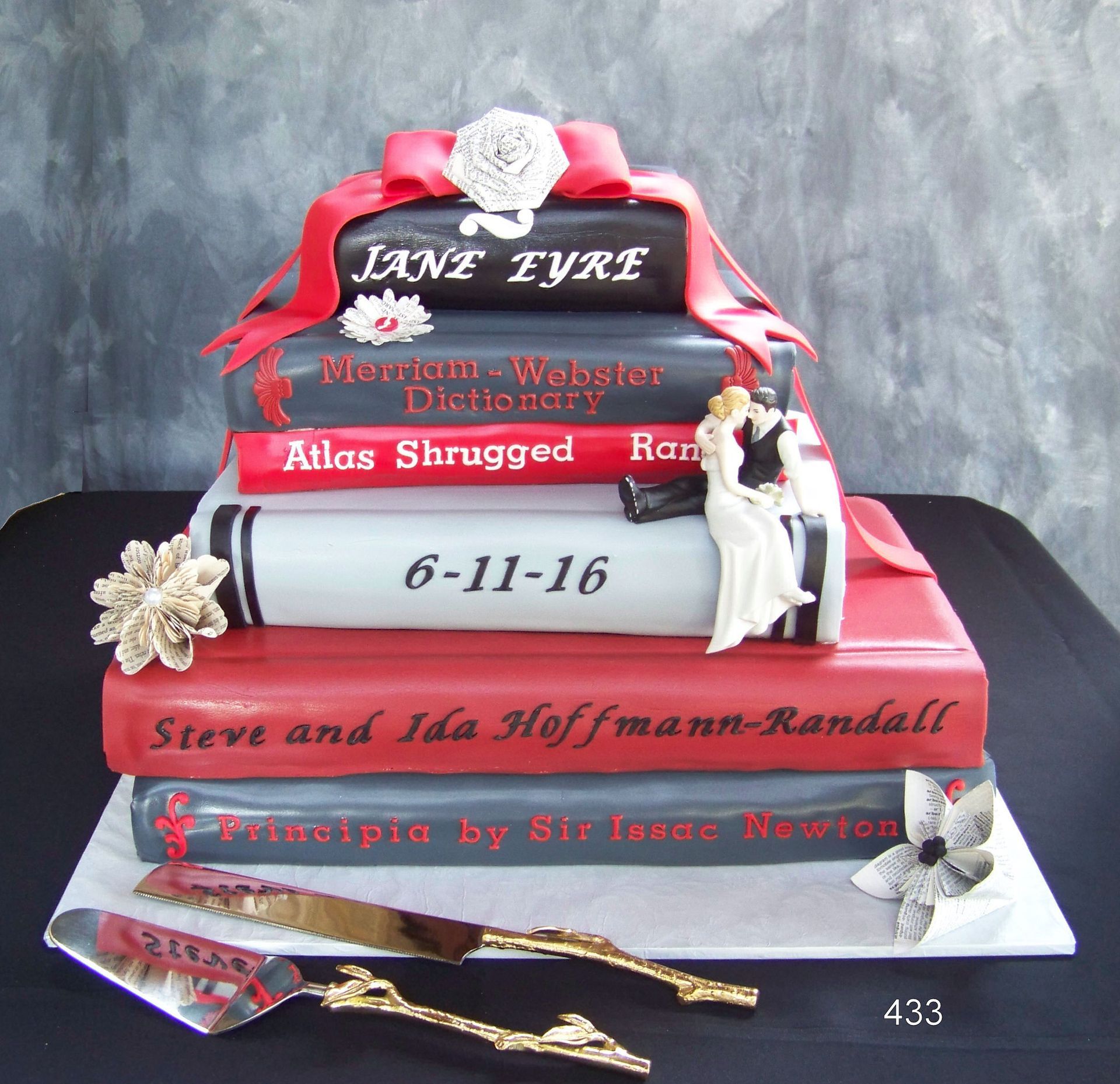 Red and black graduation cake with ribbons, flowers, and names on stacked books