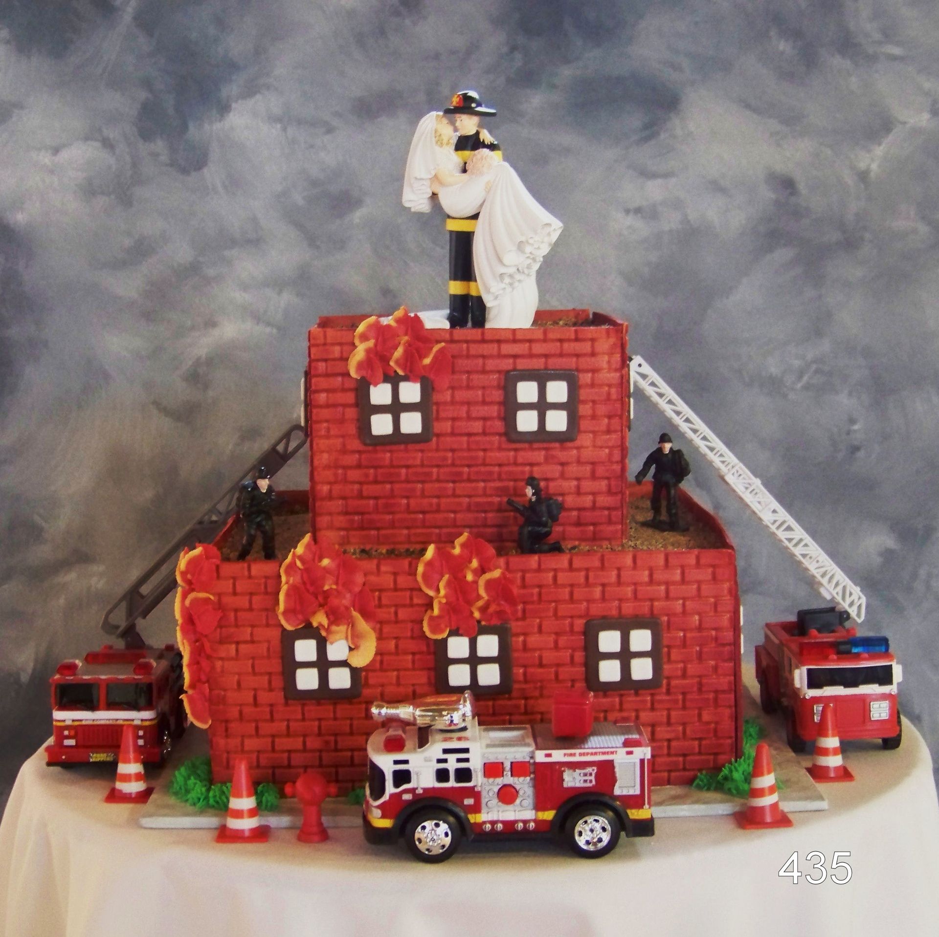 Toy fire-rescue scene with red building, flames, firefighters, and emergency vehicles under a smoky sky