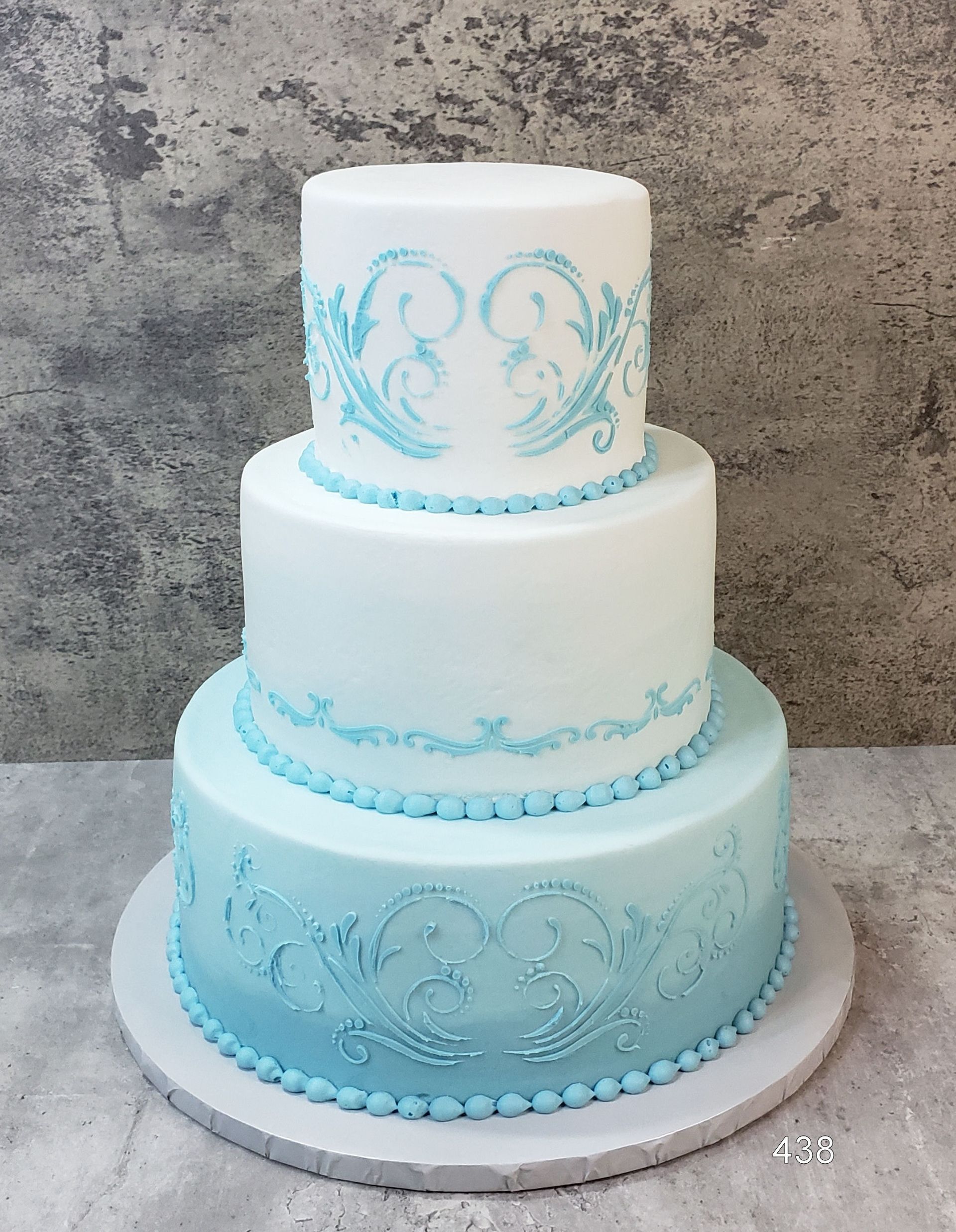 Three-tier white and aqua decorative cake with ornate piping on a silver board