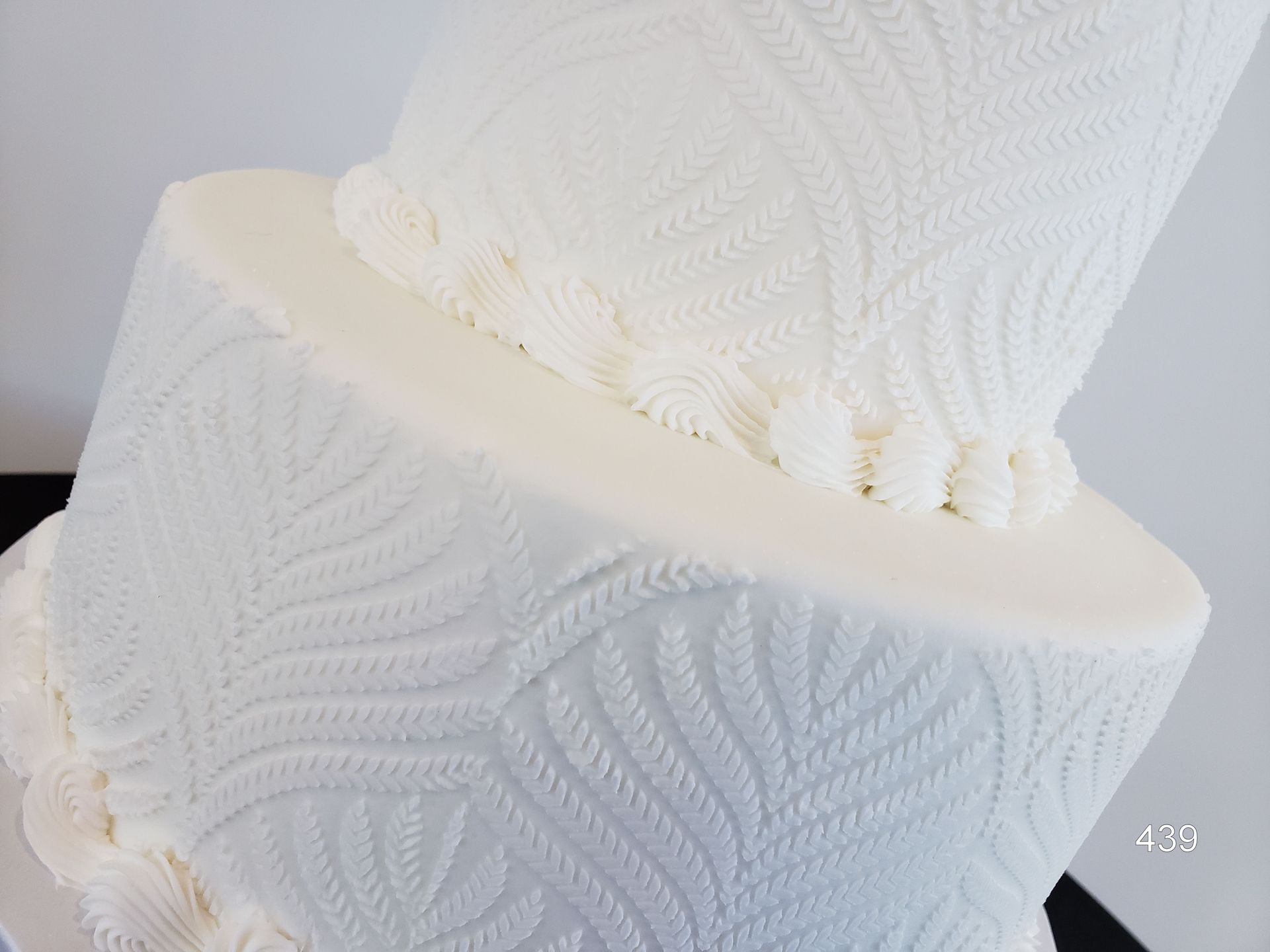 Two white fondant cakes with textured leaf patterns, stacked at an angle on a white surface.
