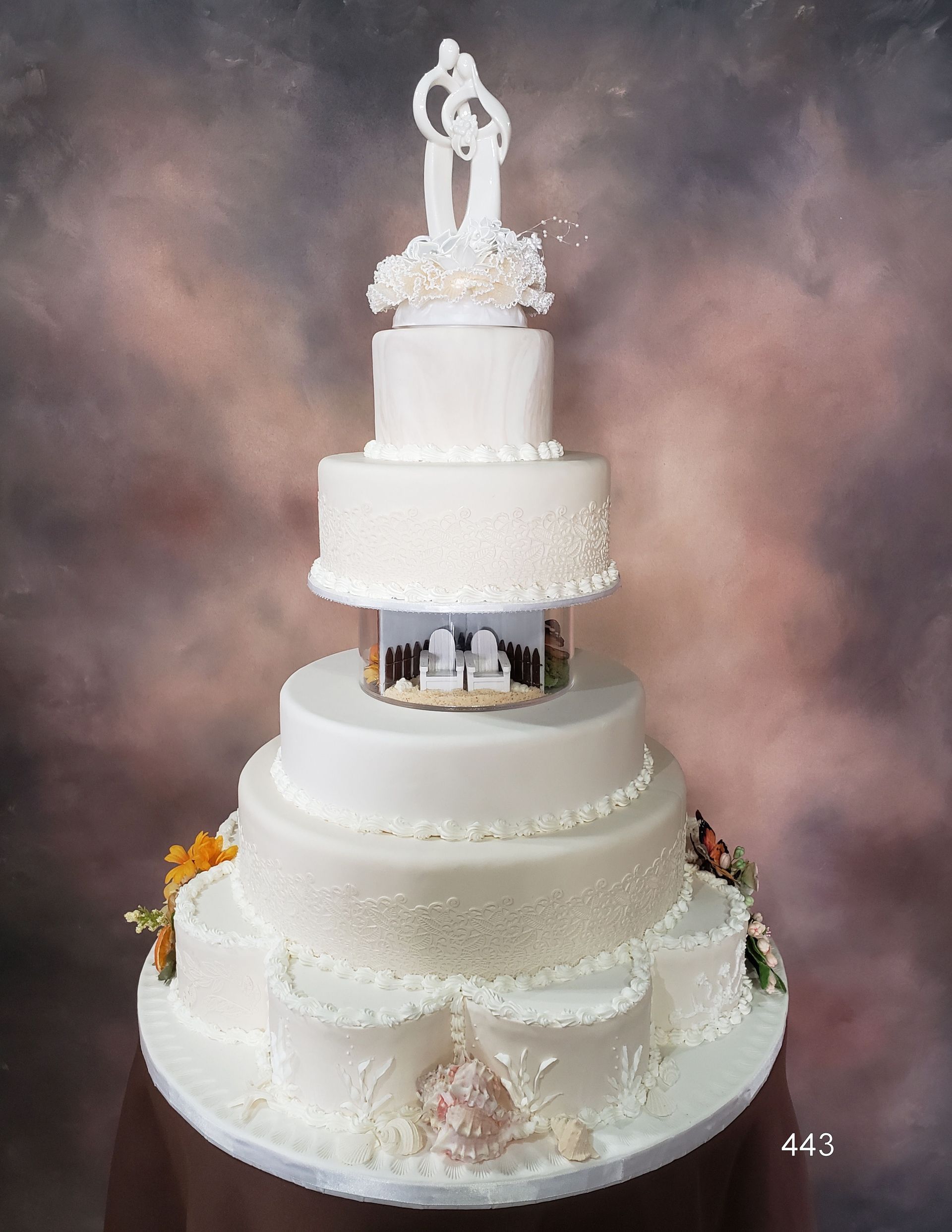 Tall white tiered wedding cake with floral accents and a bride-and-groom topper