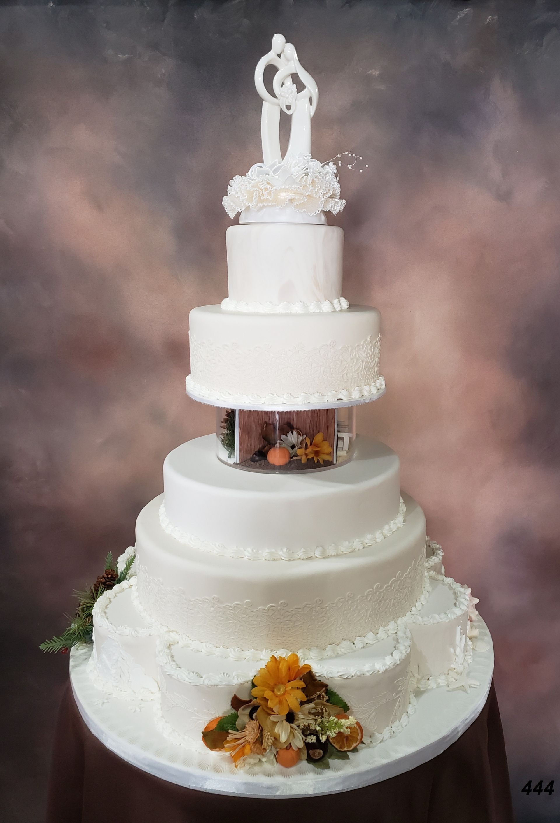 Five-tier white wedding cake with floral accents and a topper on a soft studio backdrop