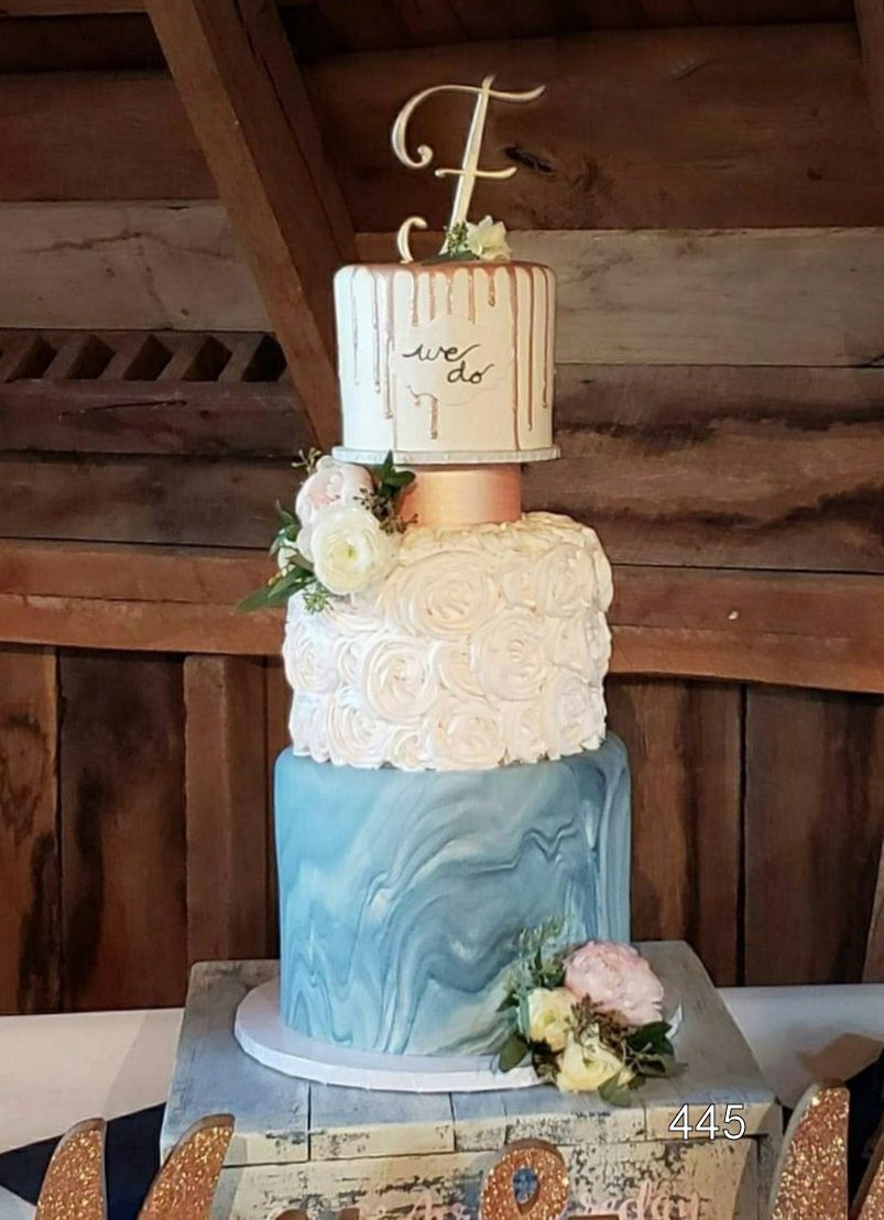 Three-tiered wedding cake with blue, white, and blush decorations in a rustic wooden venue