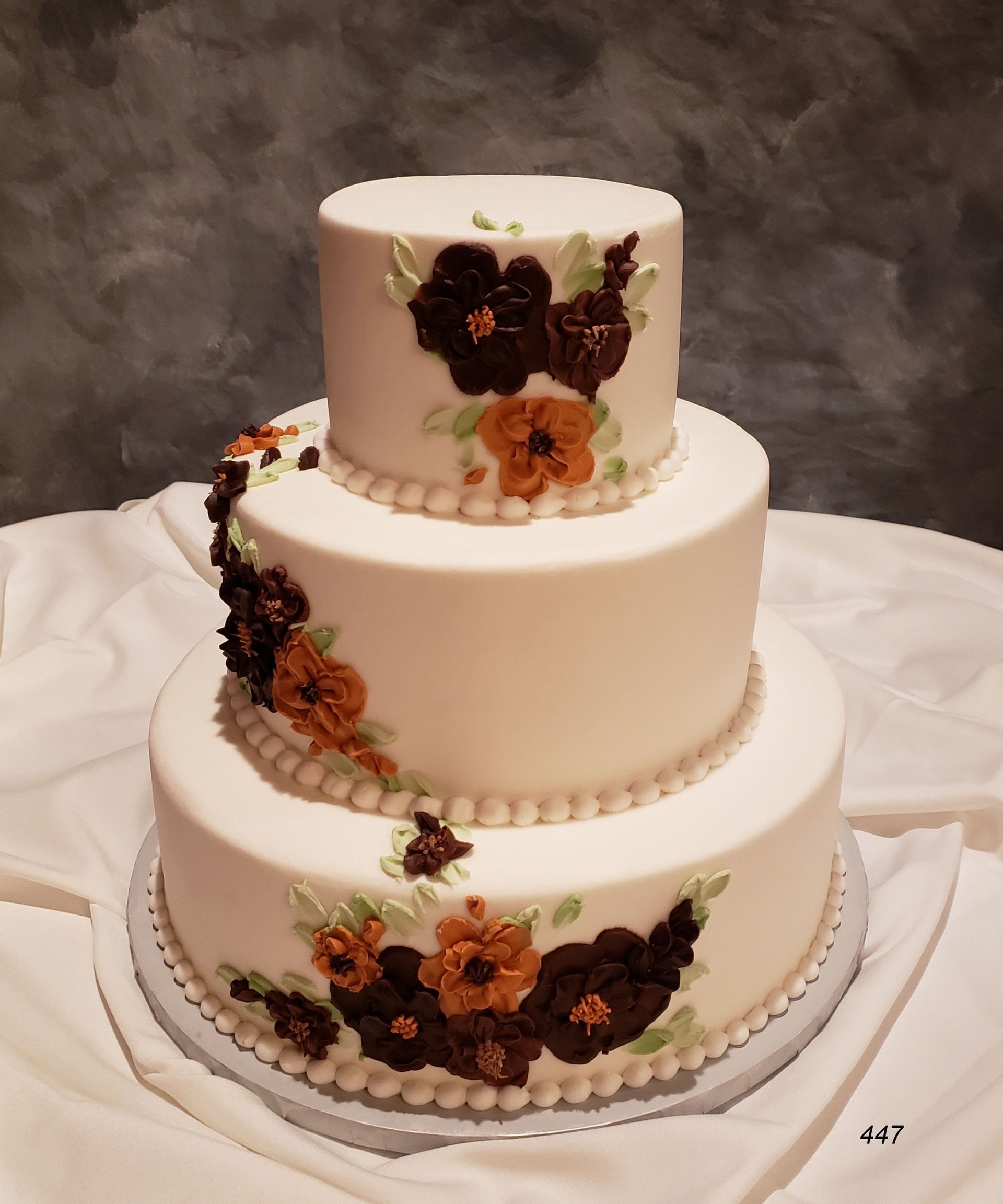 Three-tier white cake with white frosting and dark purple, orange floral decorations