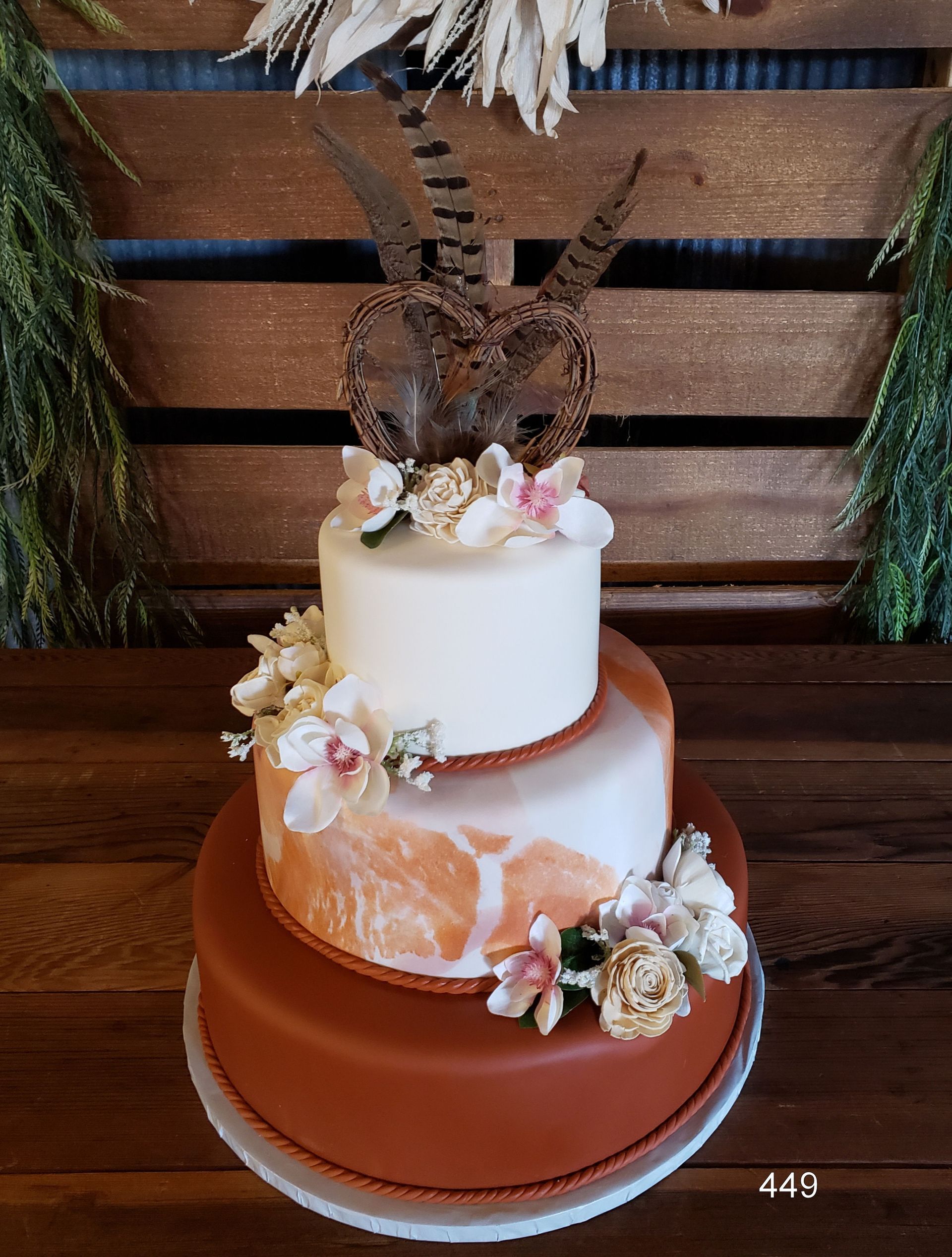 Two-tier white and peach wedding cake with flowers and gold topper on a brown stand