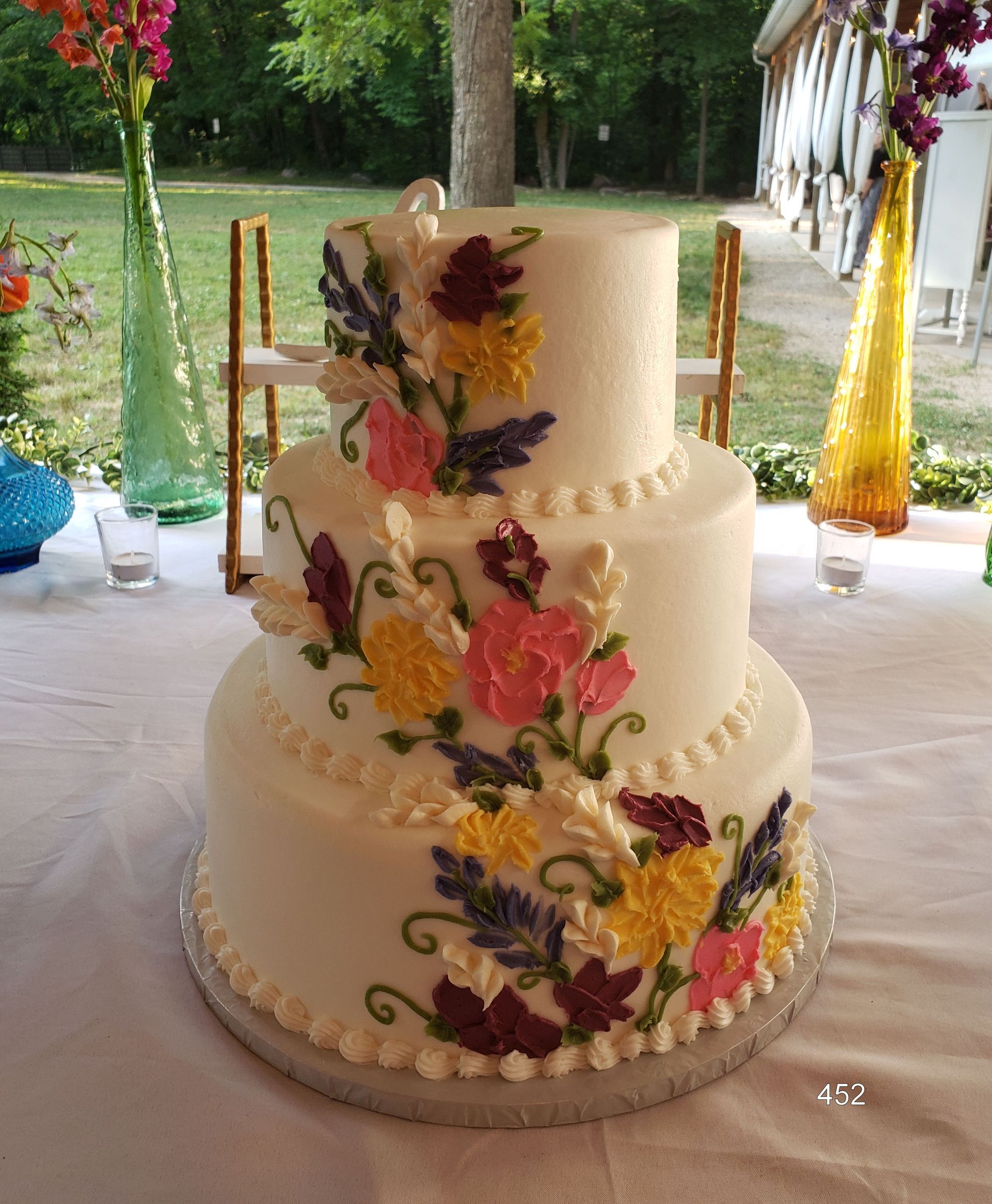 Three-tier white wedding cake with colorful floral decorations on a table outdoors