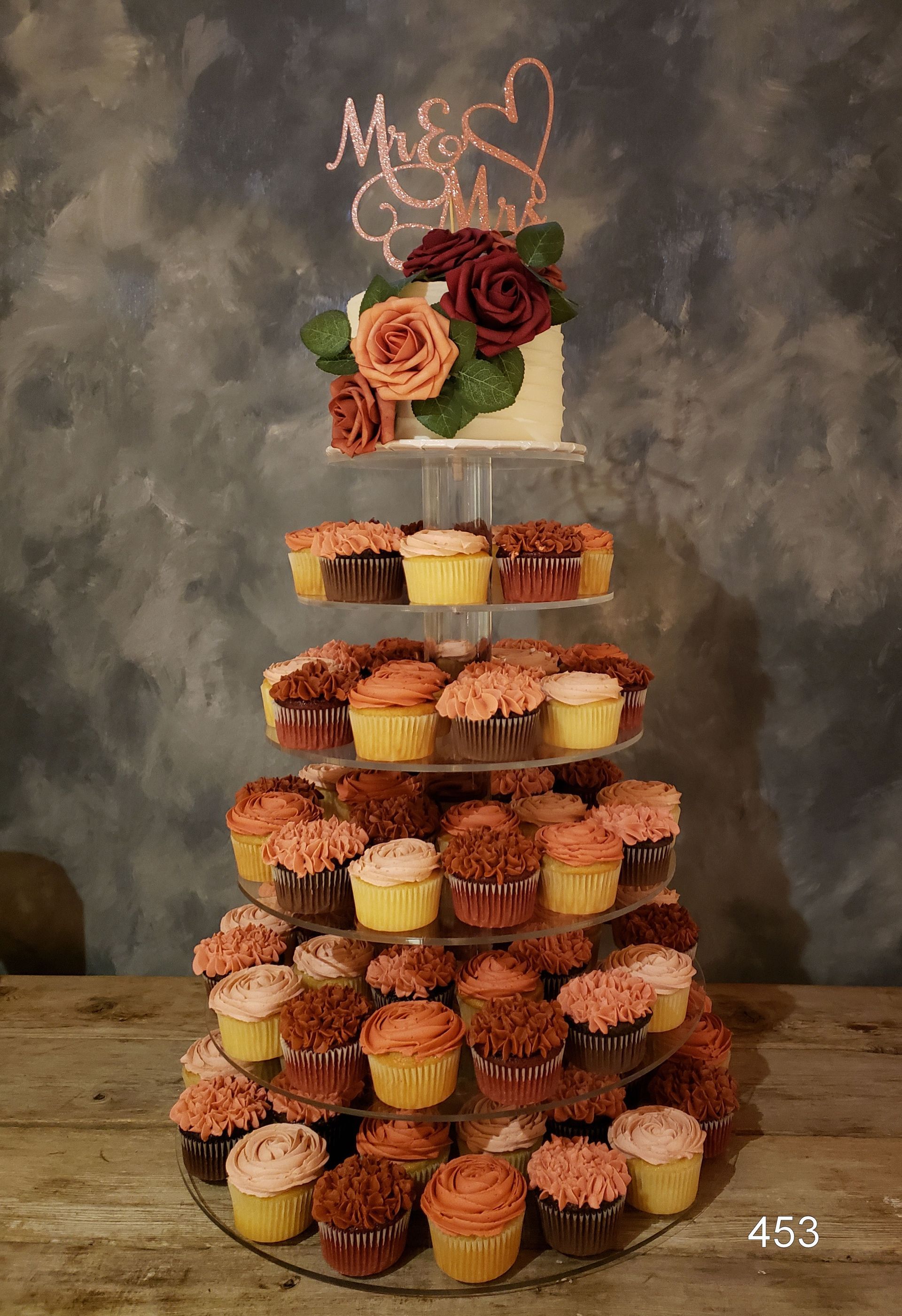 Tiered cupcake tower with pink flowers and a “Mr & Mrs” topper on a rustic table