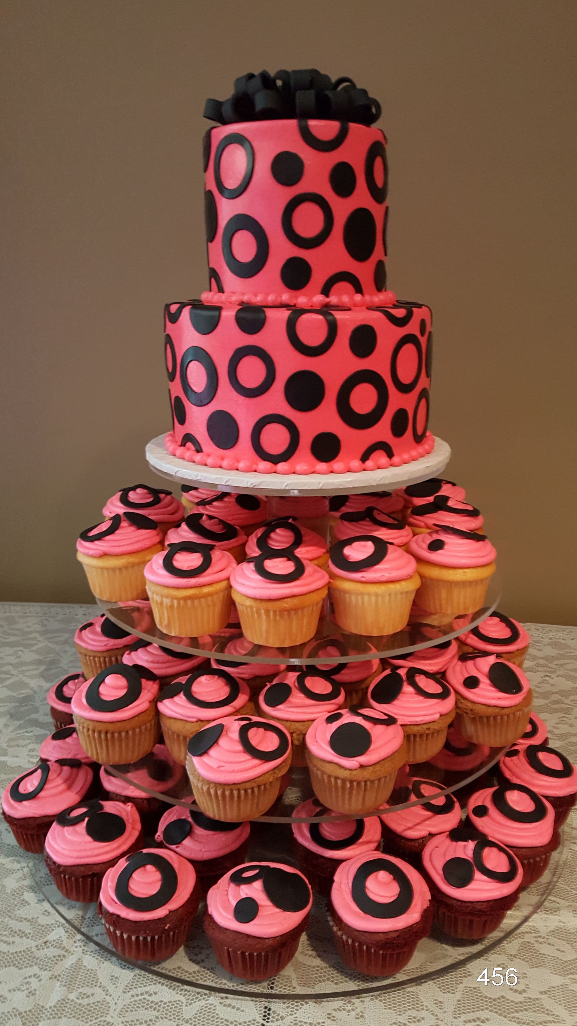 Tiered display of pink cupcakes and cakes with black polka dots, topped with black icing flowers