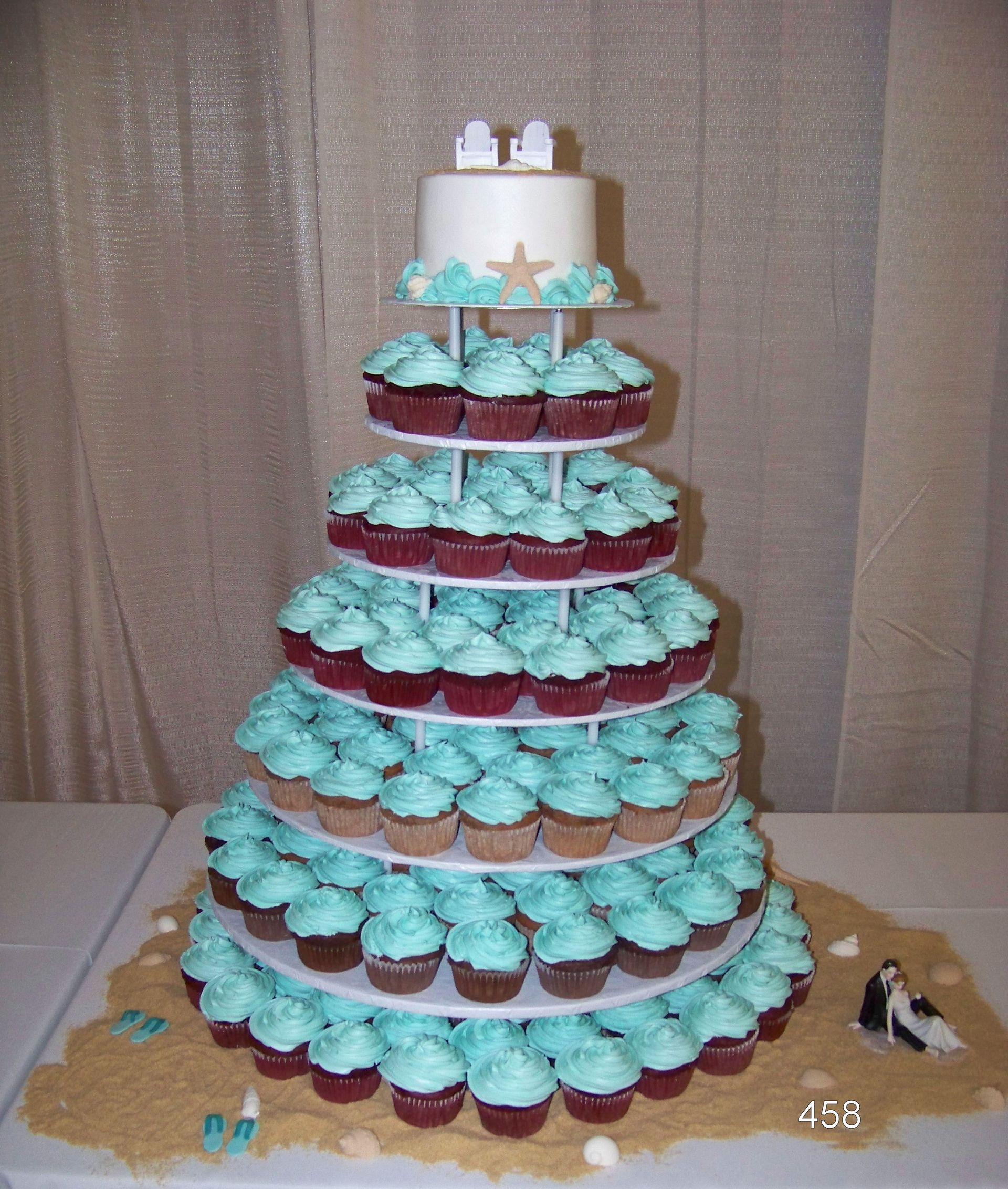 Multi-tier cupcake tower with turquoise frosting and white cake topper on a table at a party
