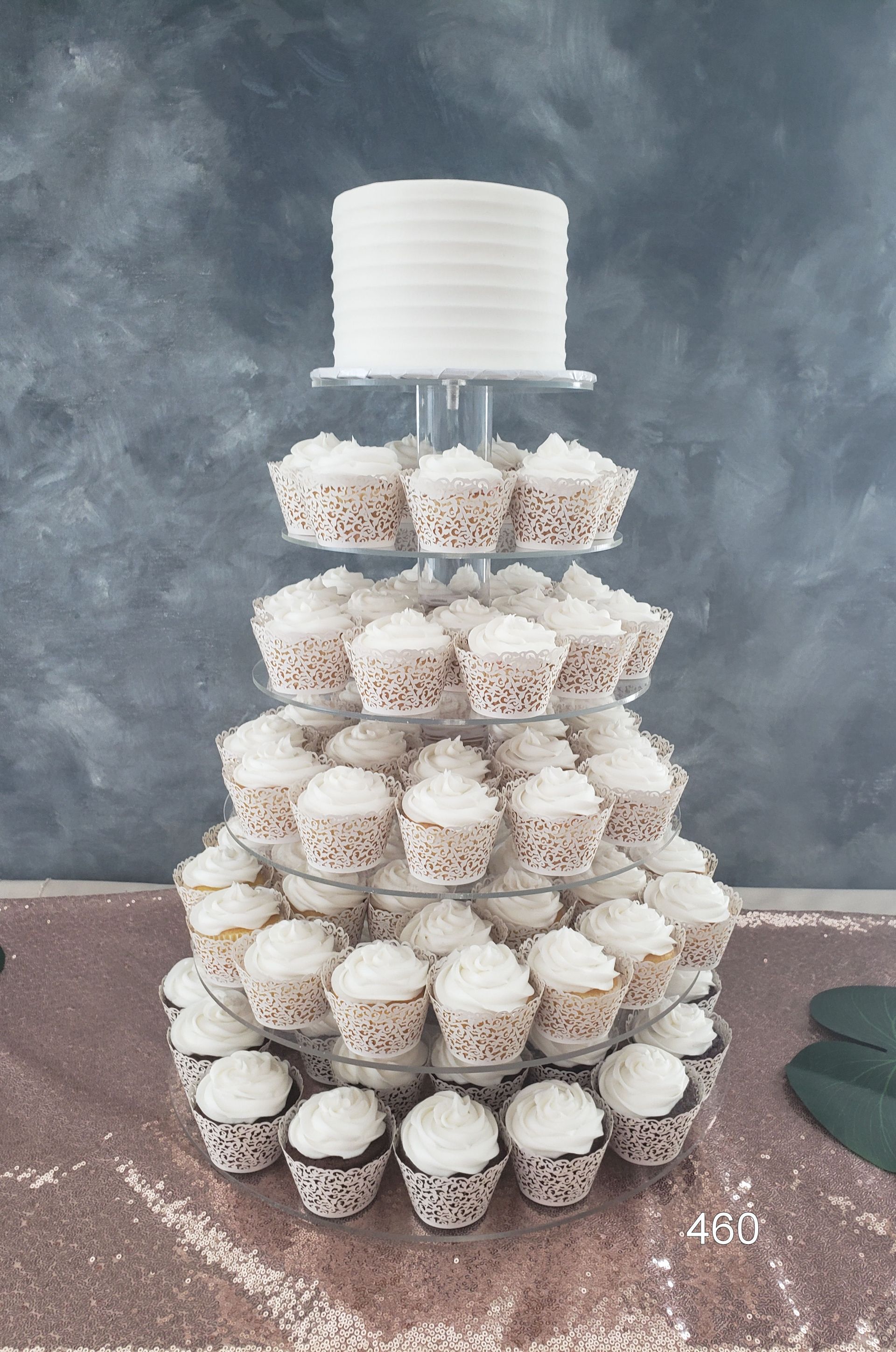 Tiered cake stand holding rows of white and speckled cupcakes against a gray wall.