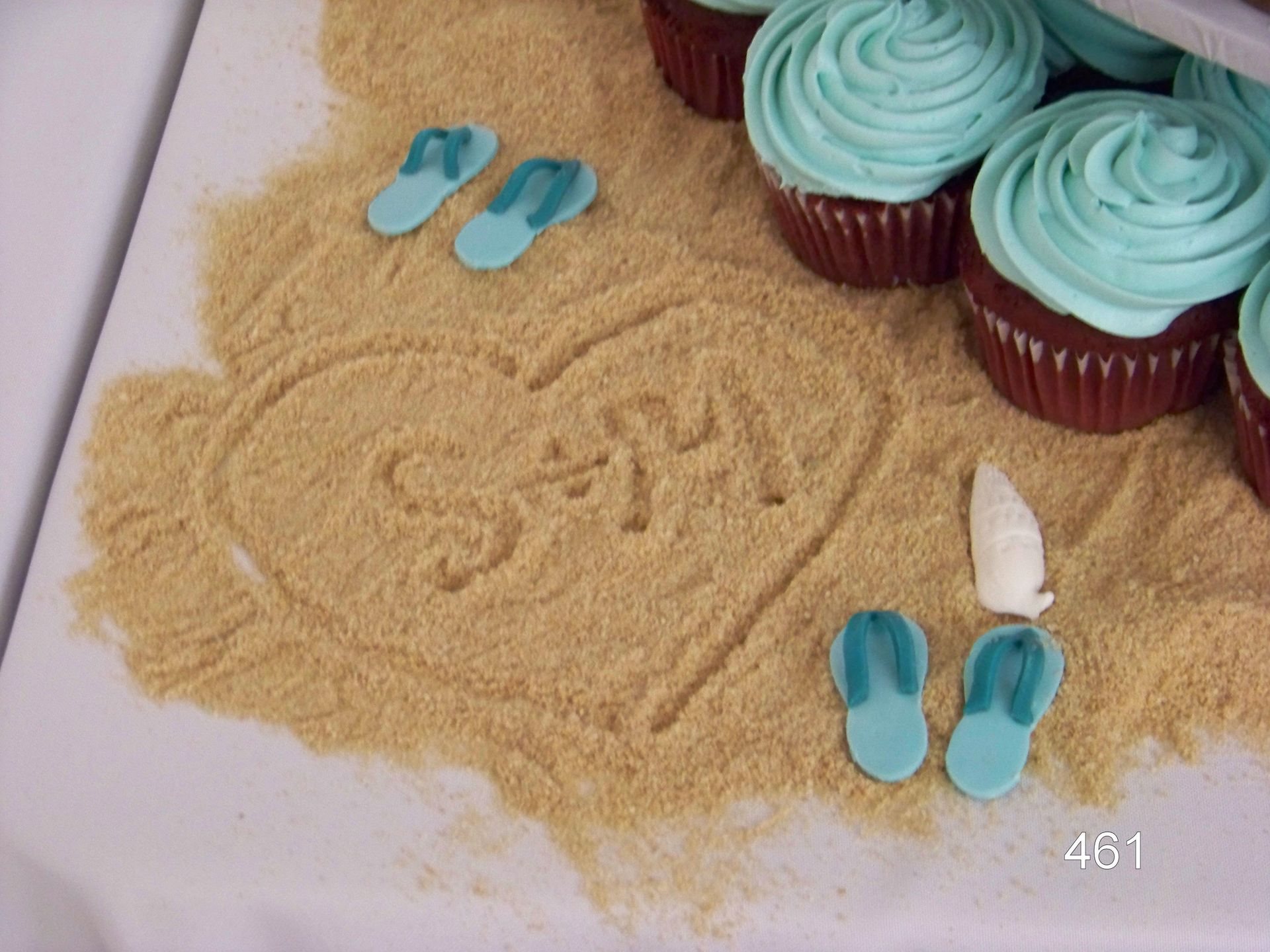 Heart-shaped sand art with the word “love,” flip-flops, and cupcakes on a beach-themed surface