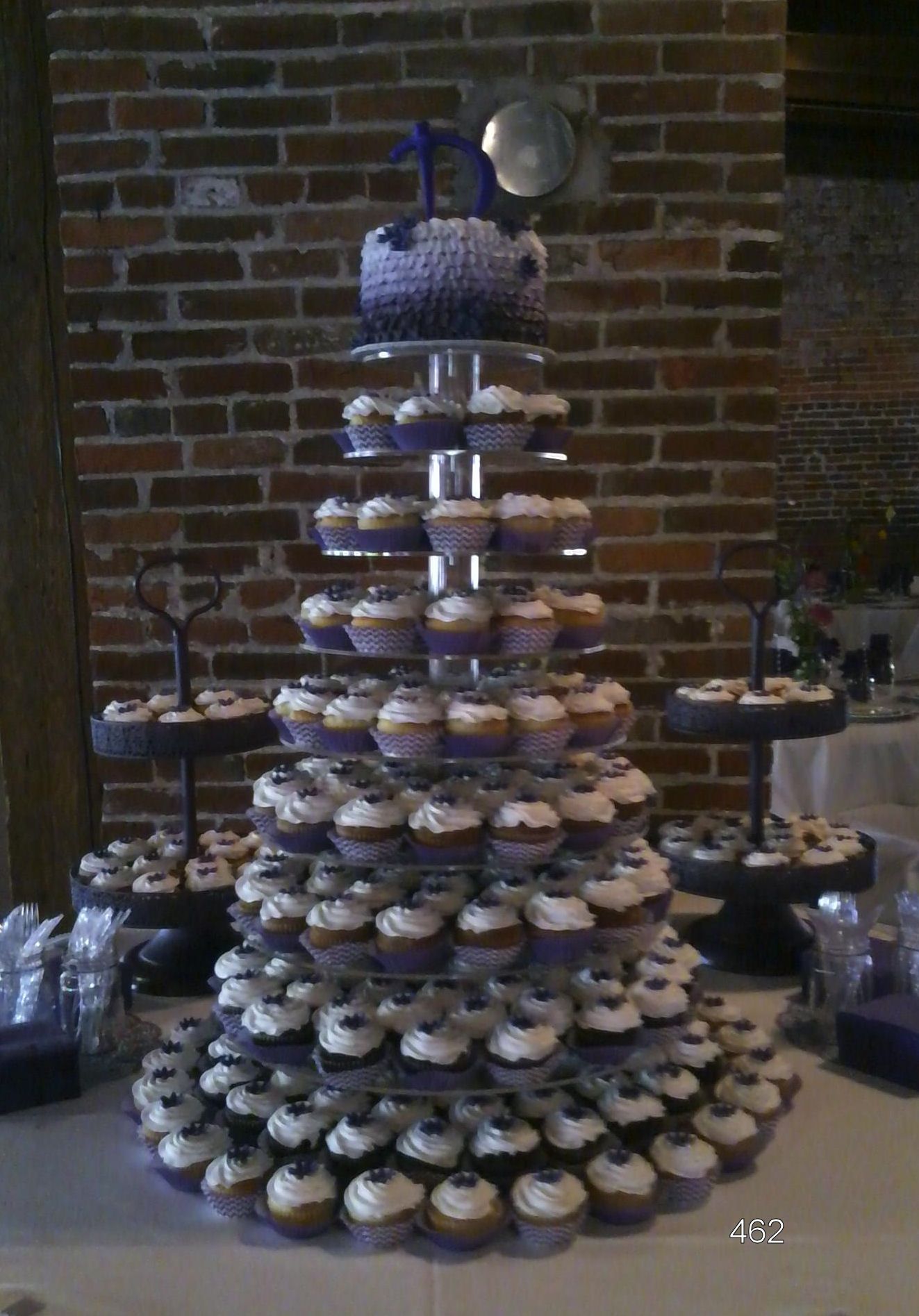Tiered display of blue-and-white cupcakes on a table against a brick wall.