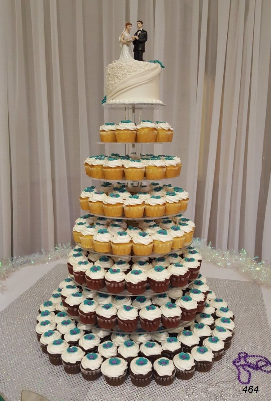 Tiered cupcake tower with a wedding topper, decorated in white, gold, and teal, on a draped backdrop