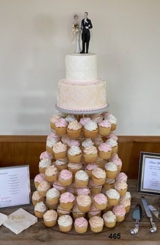 Cupcake tower wedding cake with bride and groom topper on a table, surrounded by framed signs.