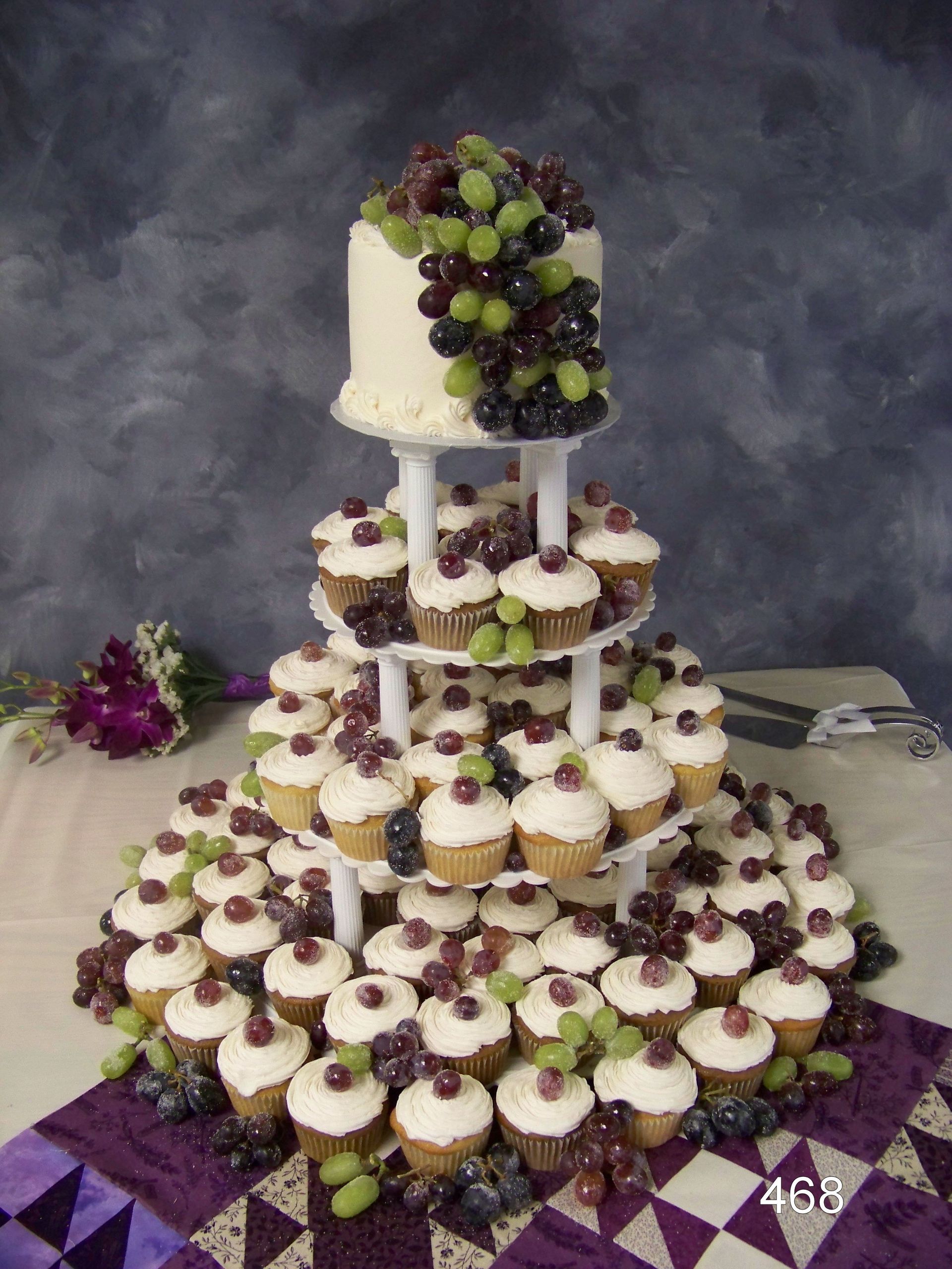 Tiered cupcake tower topped with green and purple grapes on a purple-and-black checkered tablecloth
