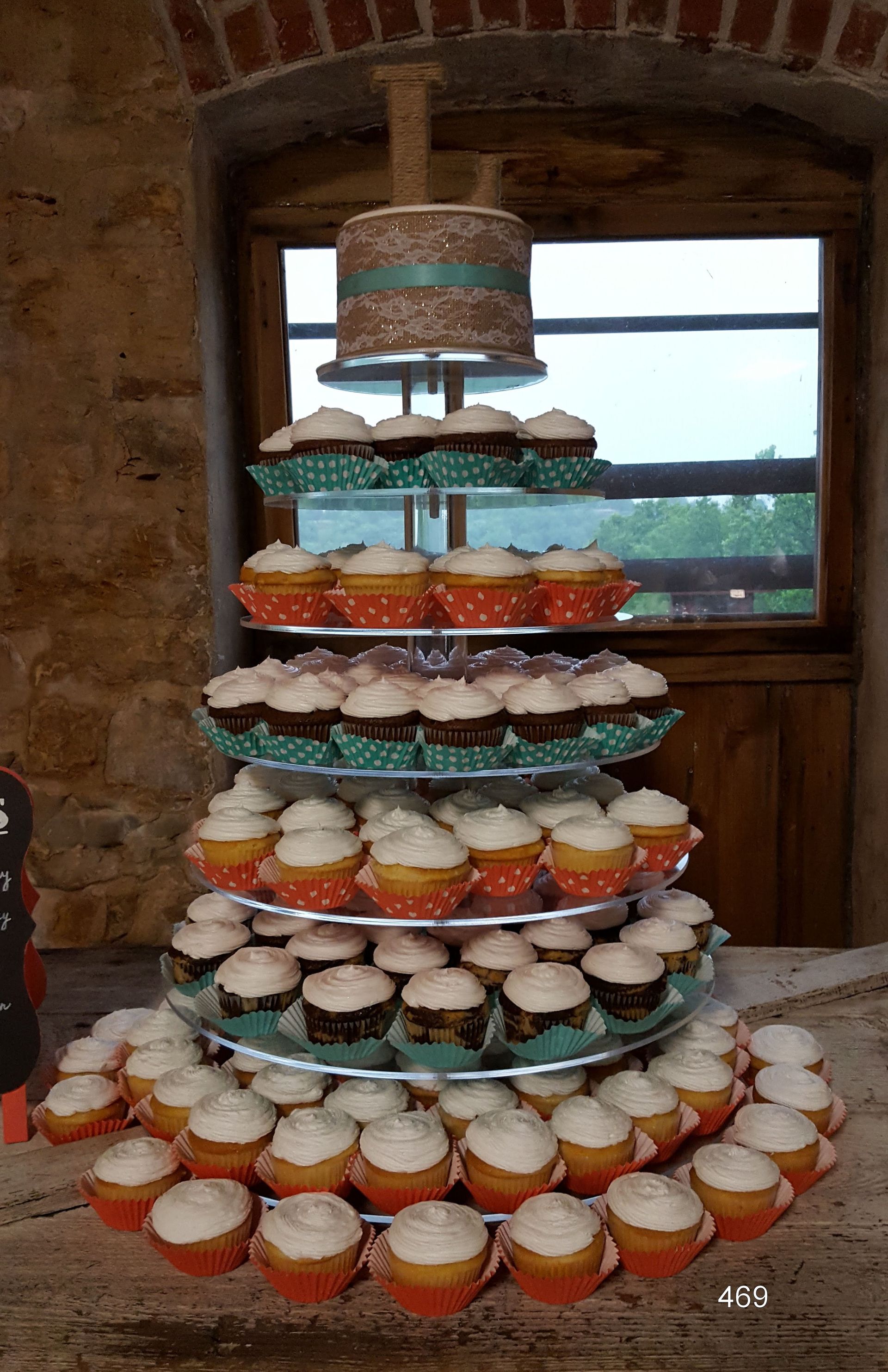 Tiered display of colorful frosted cupcakes on a wooden stand in front of a window and brick wall
