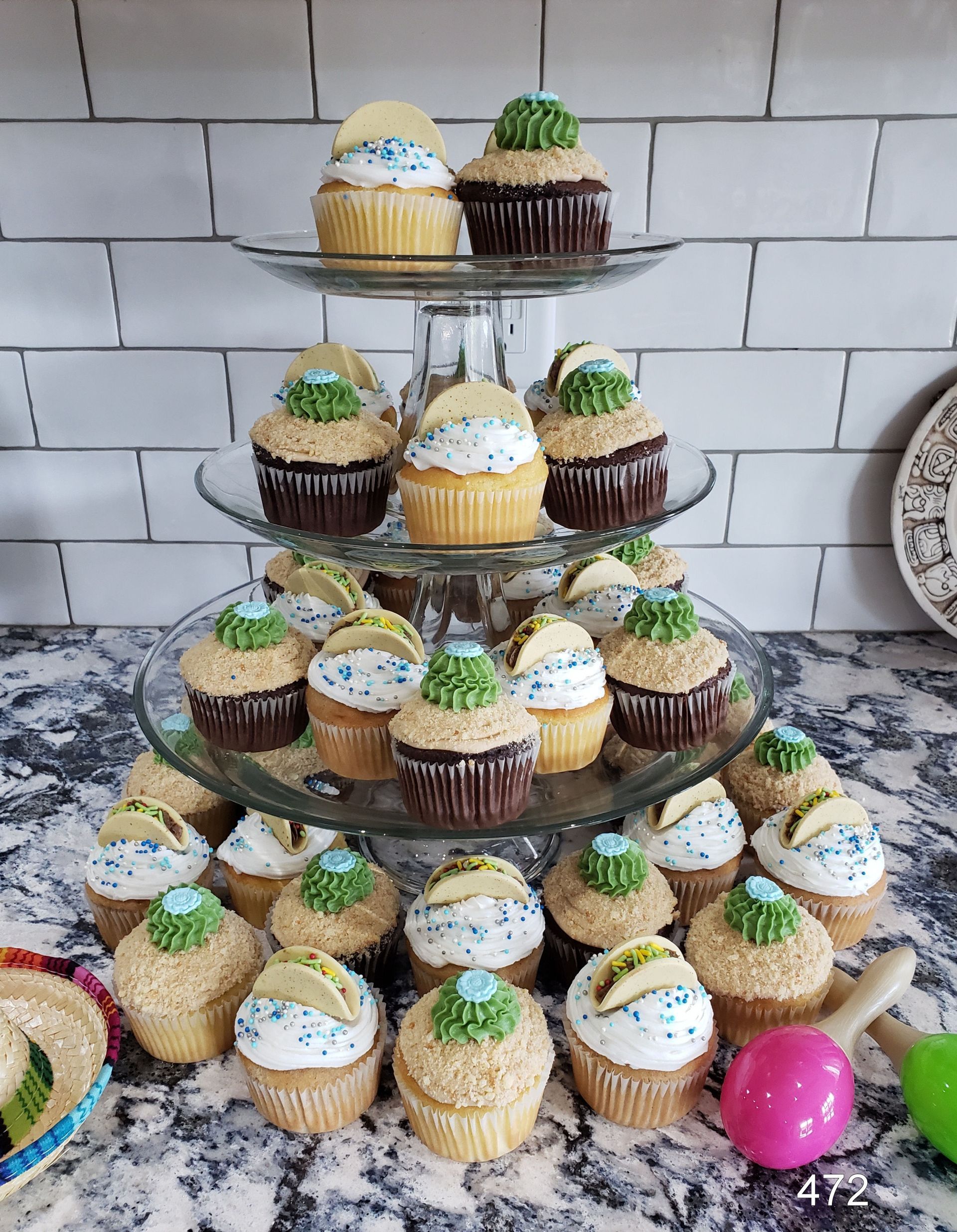 Tiered stand of decorated cupcakes with blue-and-white frosting against a white tiled wall.