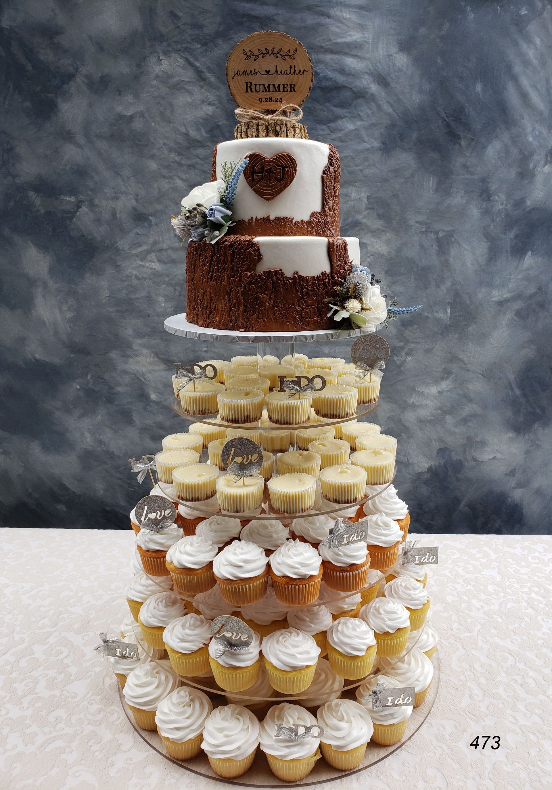 Tiered dessert tower with cupcakes and assorted treats on a white table against a gray backdrop