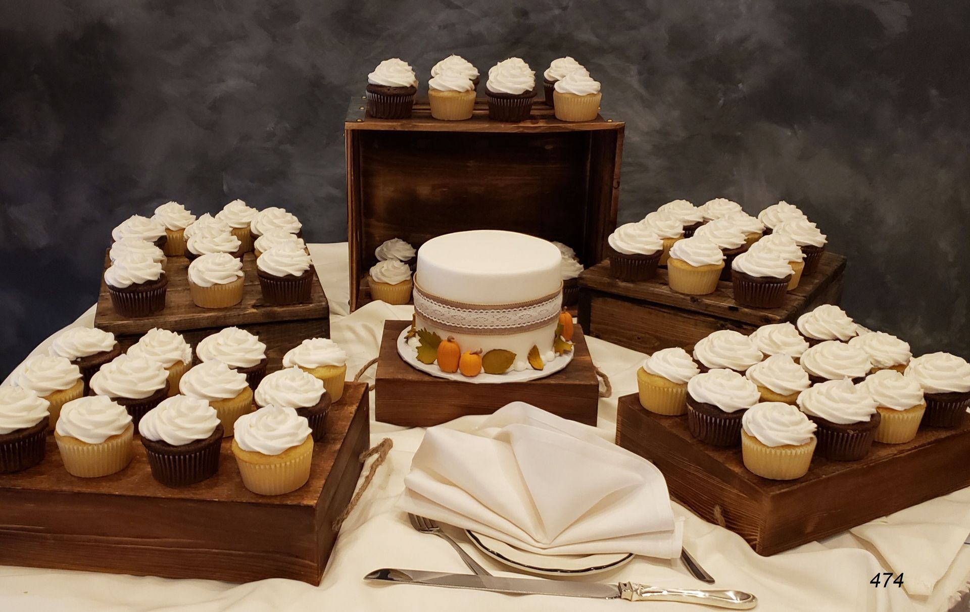 Assorted cupcakes and a tiered cake on wooden stands with a folded napkin centerpiece