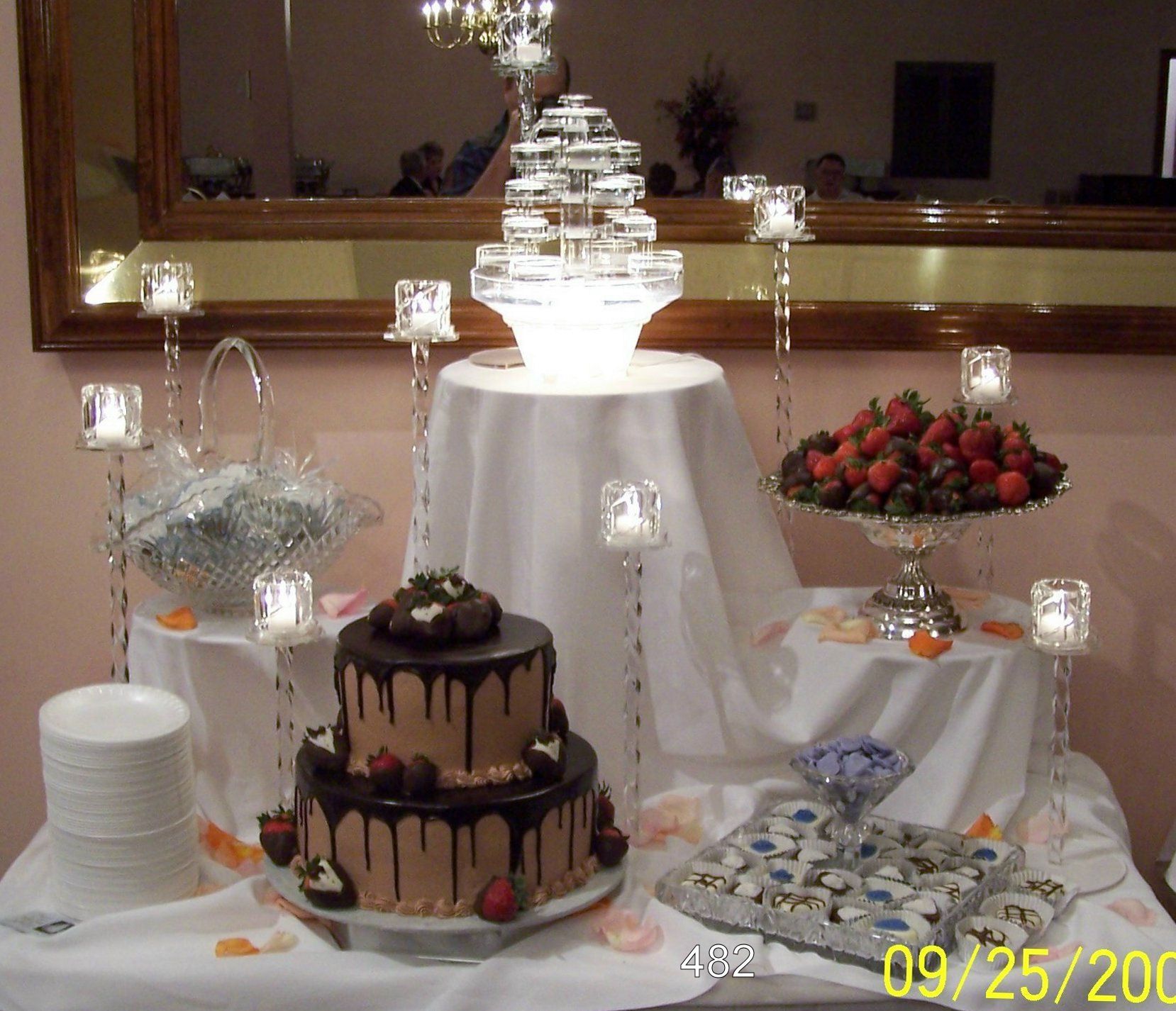 Dessert display with wedding cake, chocolate cake, strawberries, and white table decor under a mirror backdrop