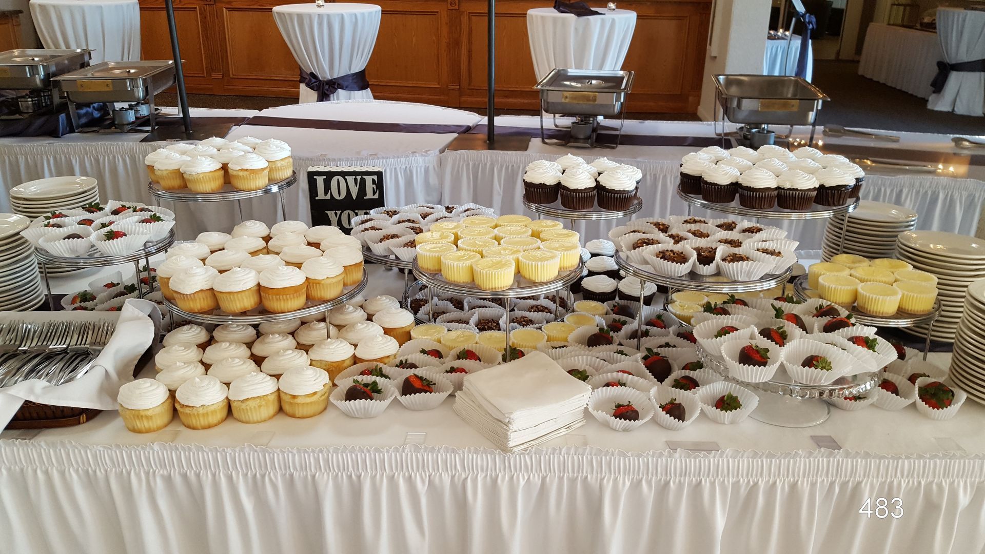 Dessert buffet with cupcakes and pastries arranged on a white tablecloth, labeled “LOVE.”