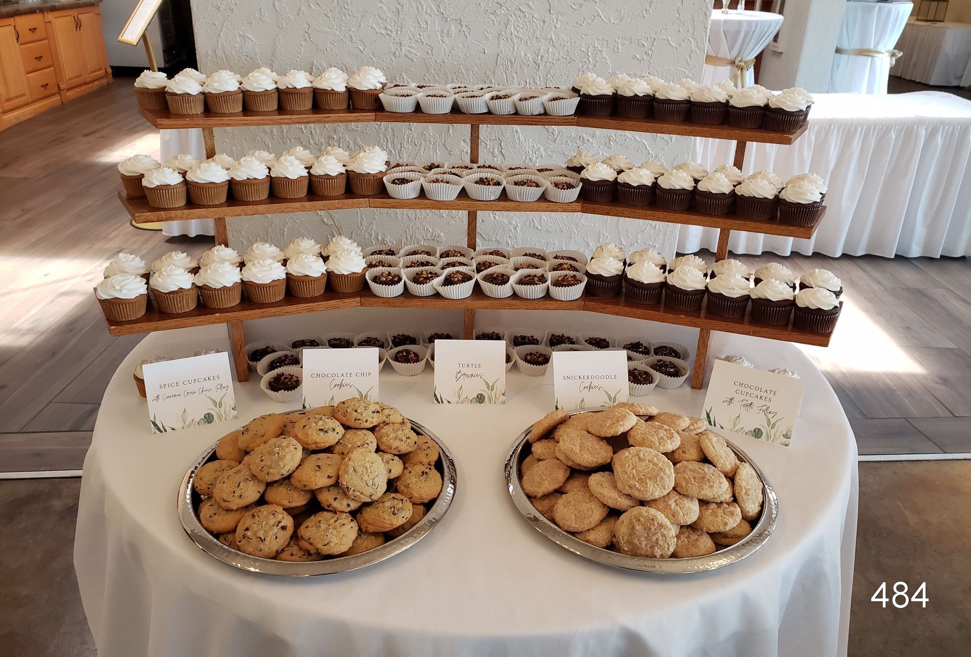 Dessert display table with tiered cupcakes and two large platters of cookies at an event.