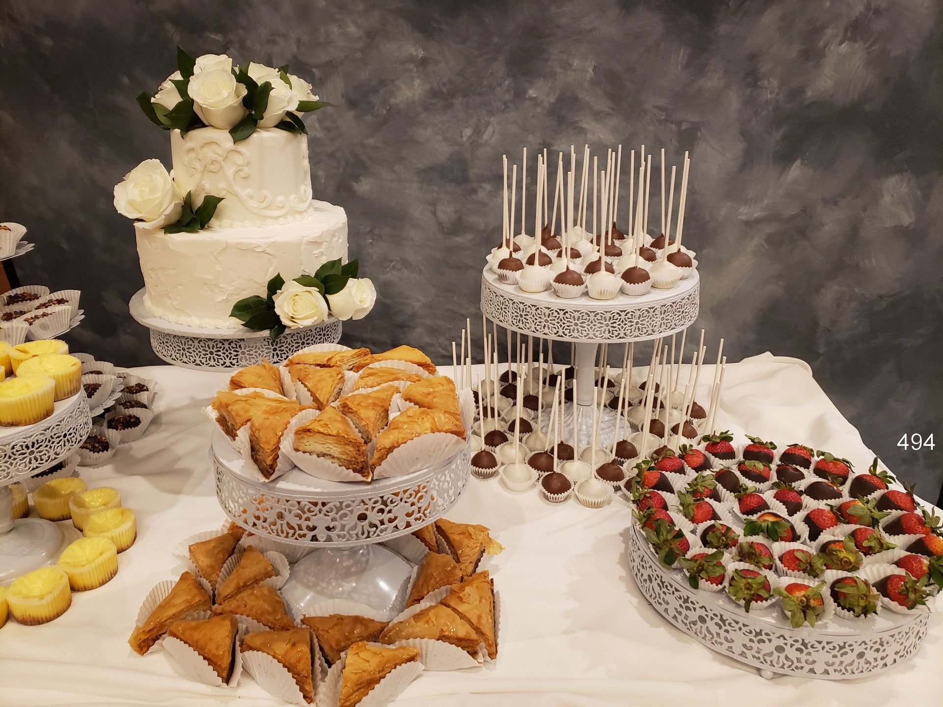 Dessert table with a tiered white cake, pastries, and fruit-topped sweets on lace stands and platters