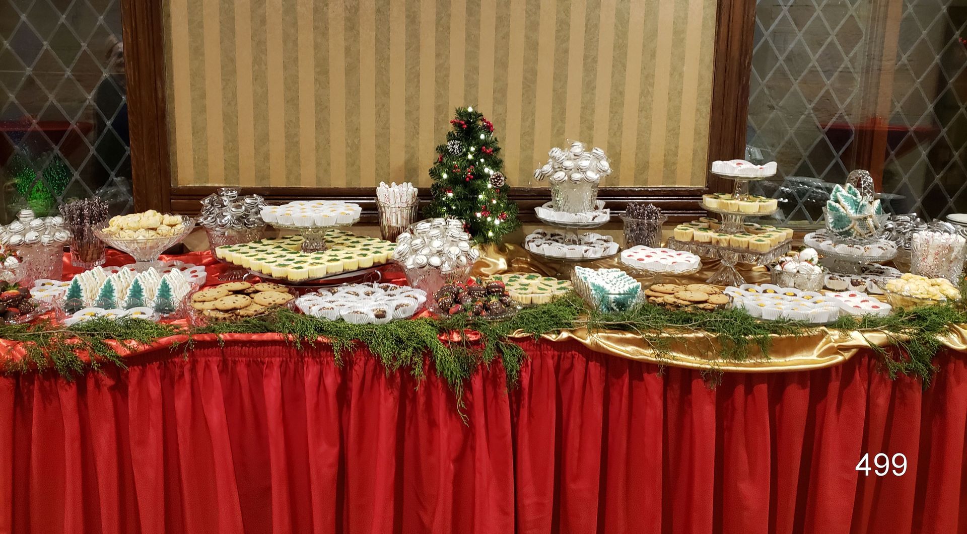 Buffet table with assorted desserts and fruit, decorated with red skirting and greenery