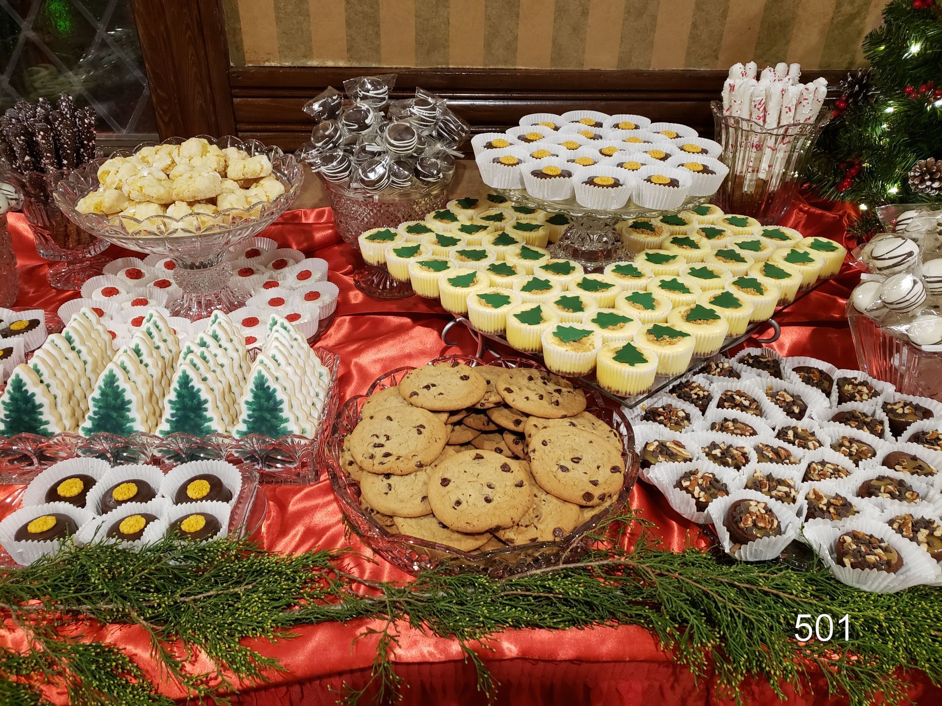 Assorted holiday cookies arranged on a red tablecloth with festive greenery and foil decorations