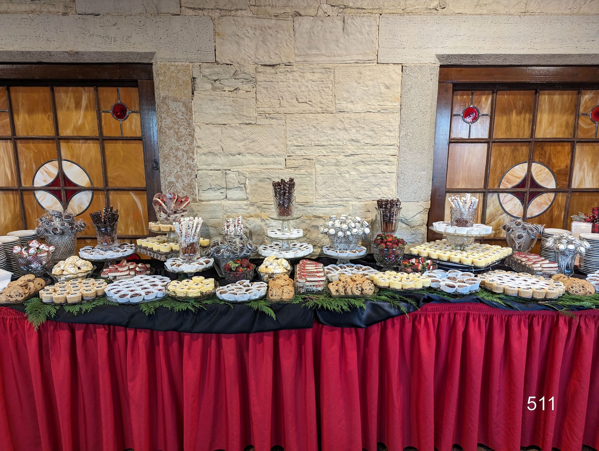 Buffet table with assorted desserts and pastries, decorated with black and red tablecloths against a stone wall