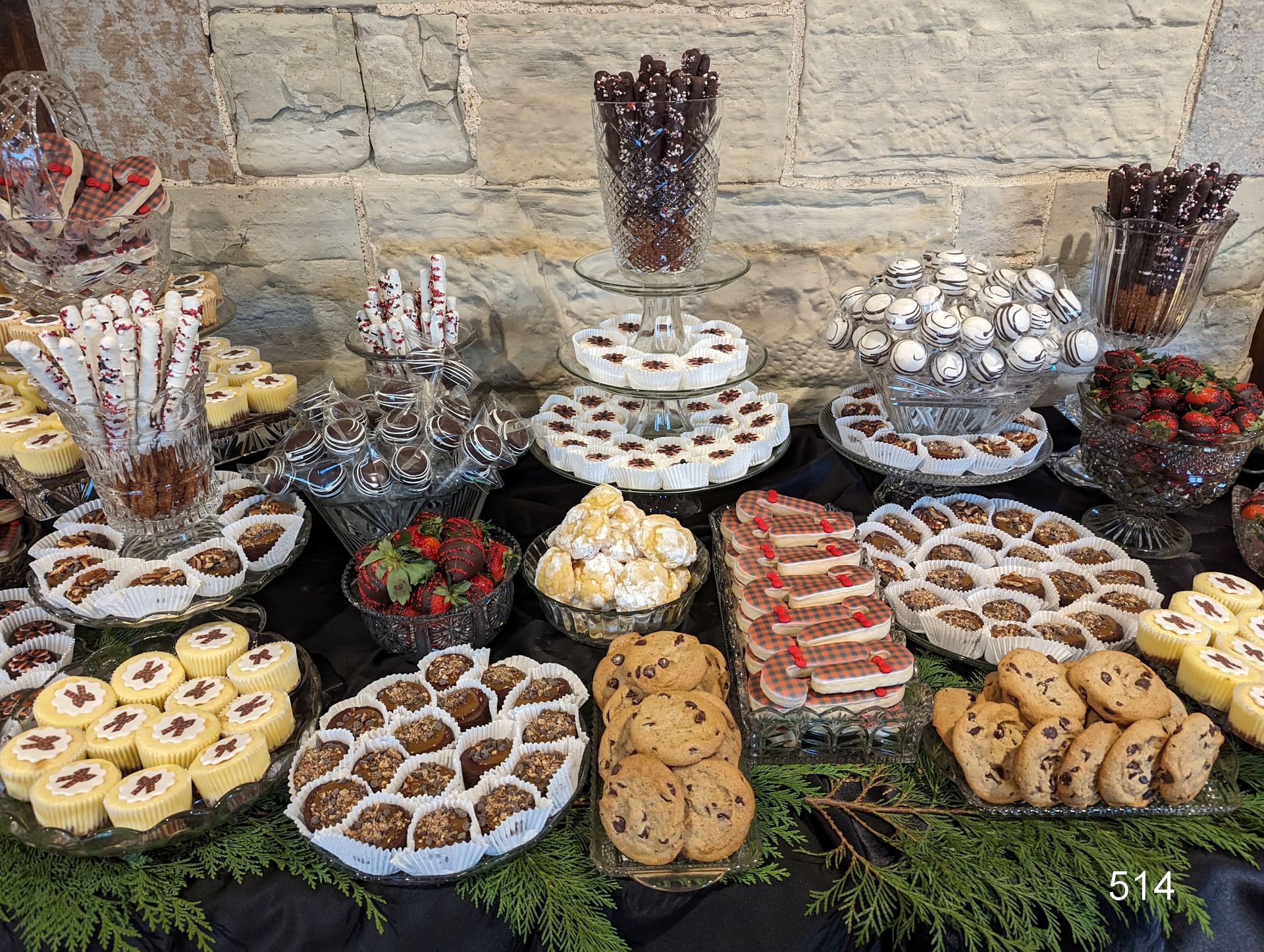 Assorted colorful pastries and desserts displayed on a table against a stone wall.