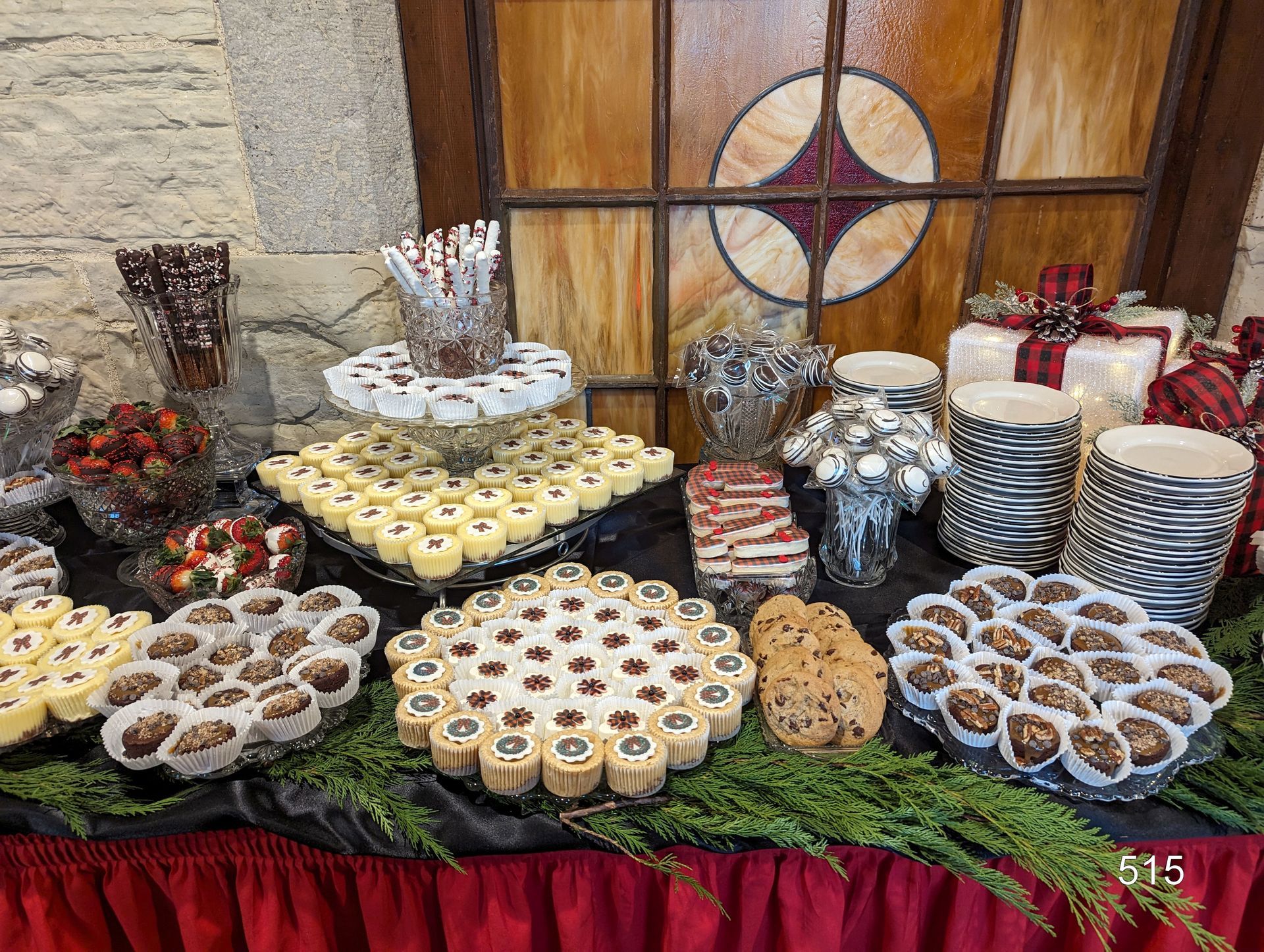 Assorted cupcakes and pastries arranged on a table with decorative greenery and stone wall backdrop