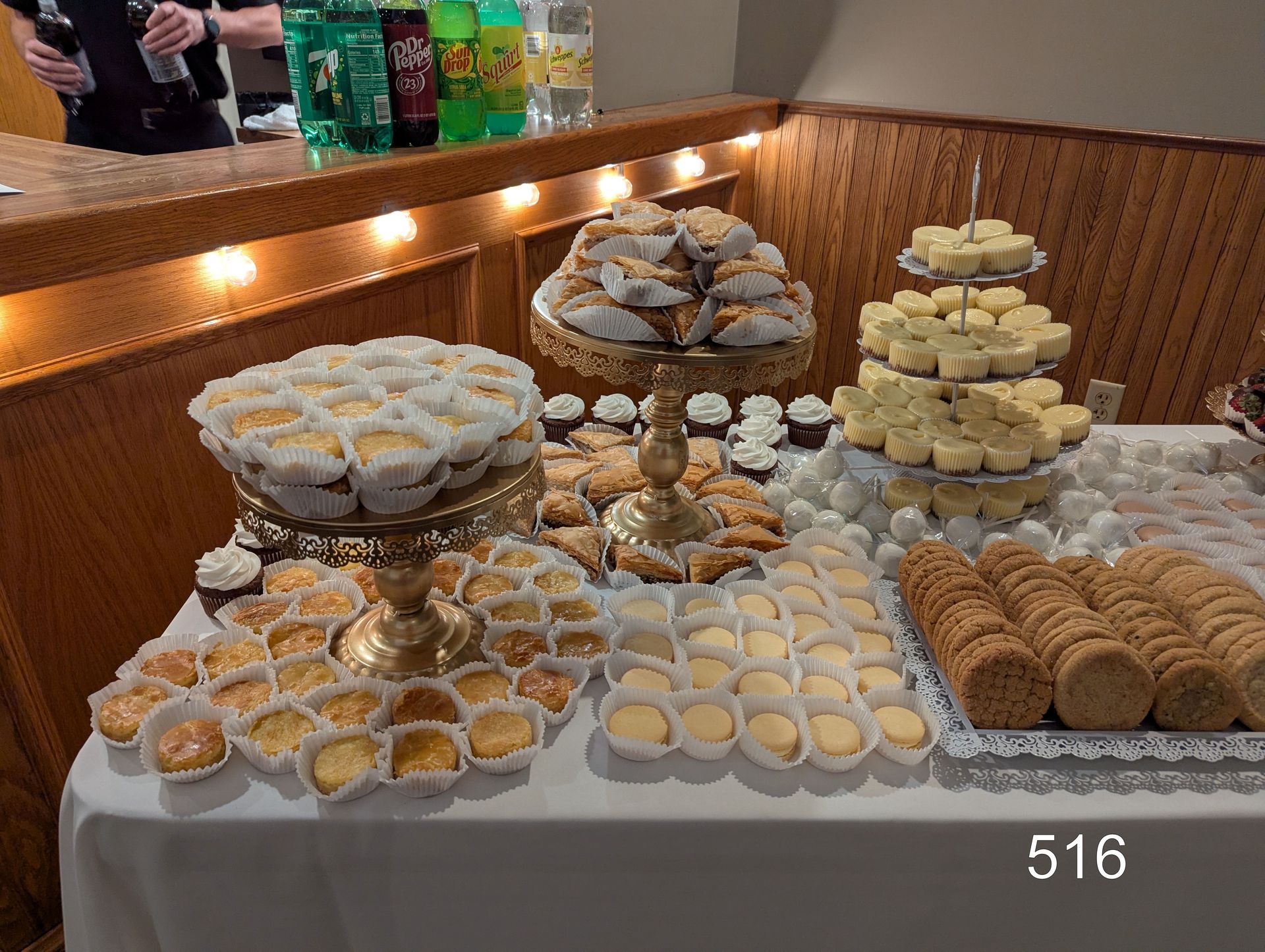 Dessert buffet with assorted pastries, cookies, and cupcakes arranged on tiered trays in a wooden room.